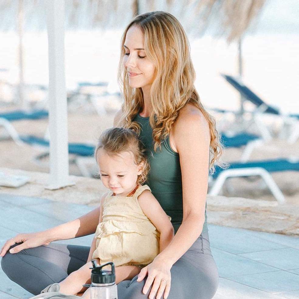 Lauren Eckstrom relaxes in a seated meditation position with her toddler-aged daughter on her lap.