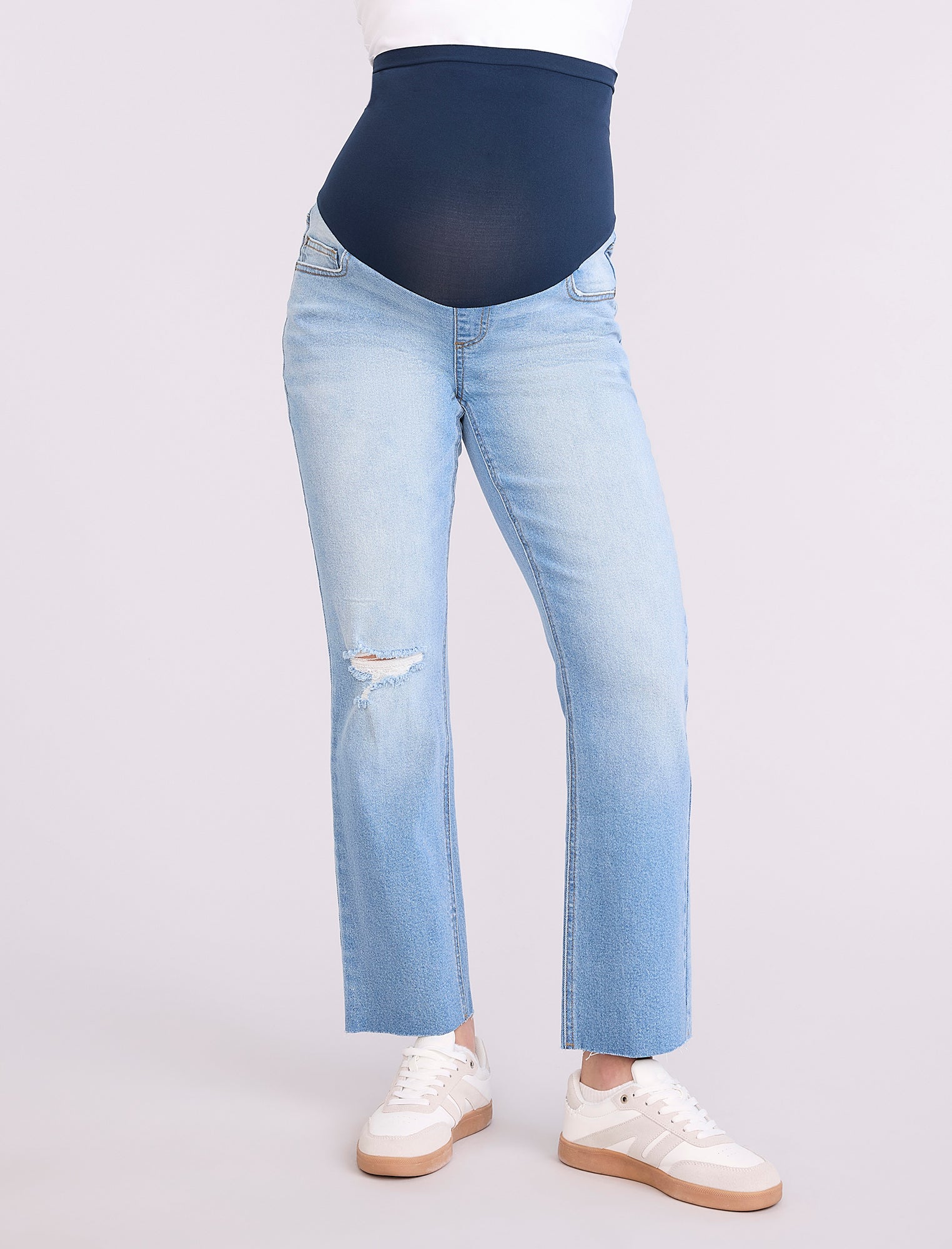 Pregnant woman wearing light blue jeans on a neutral background