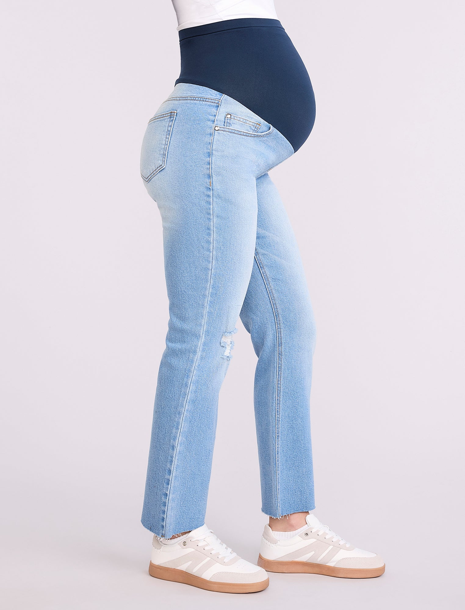 Pregnant woman wearing light blue jeans on a neutral background
