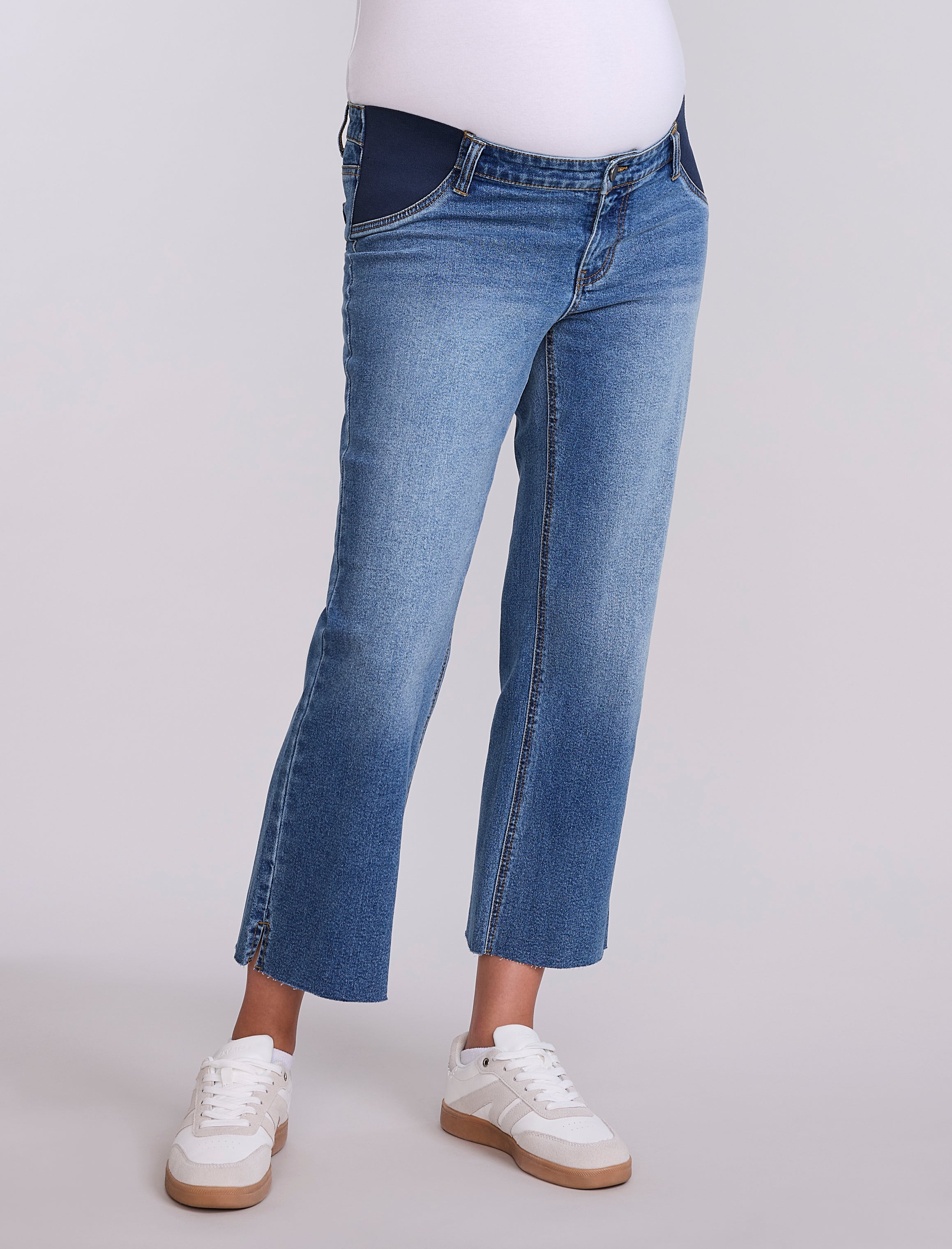 Person wearing maternity blue jeans and white sneakers on a light gray background