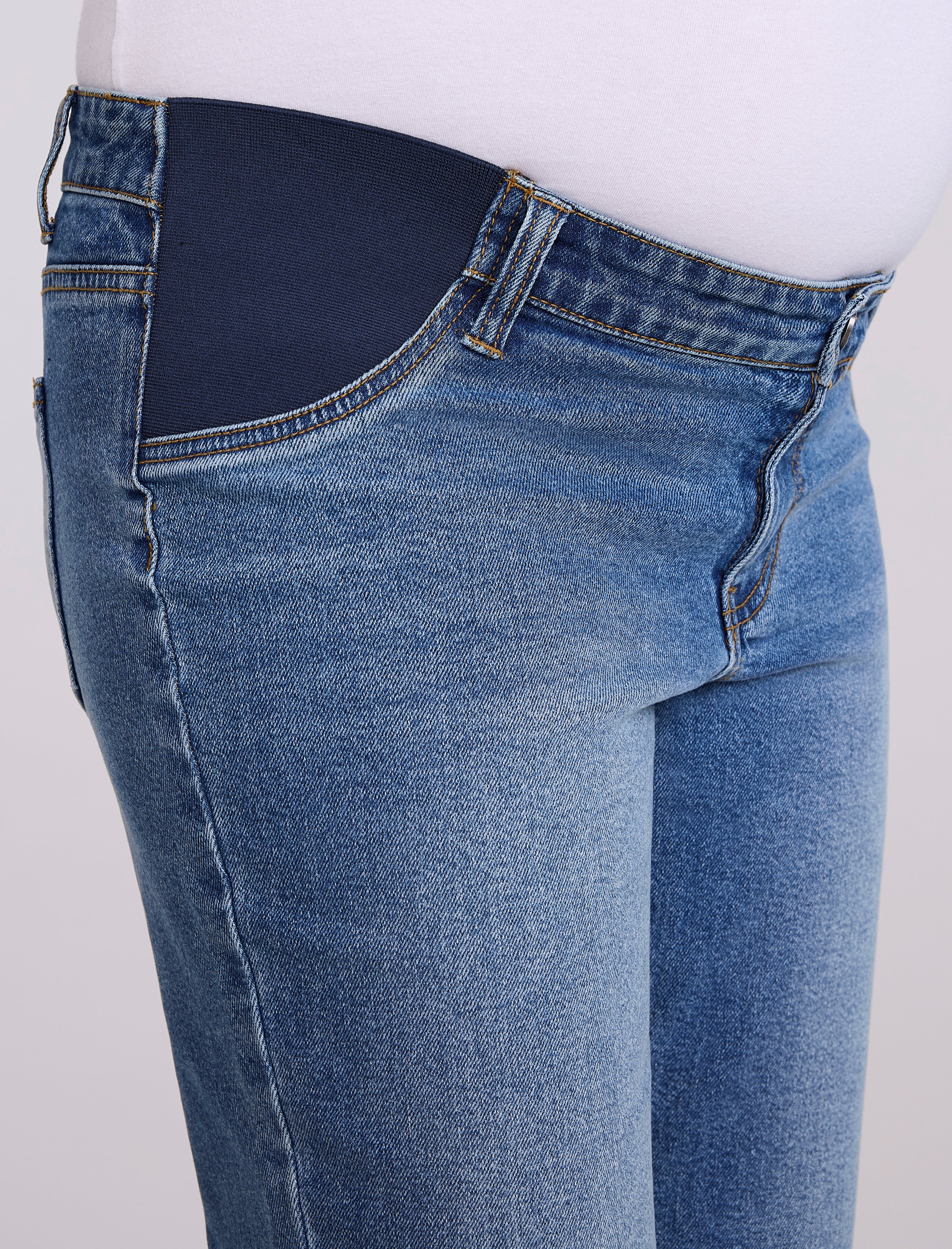 Person wearing maternity blue jeans and white sneakers on a light gray background