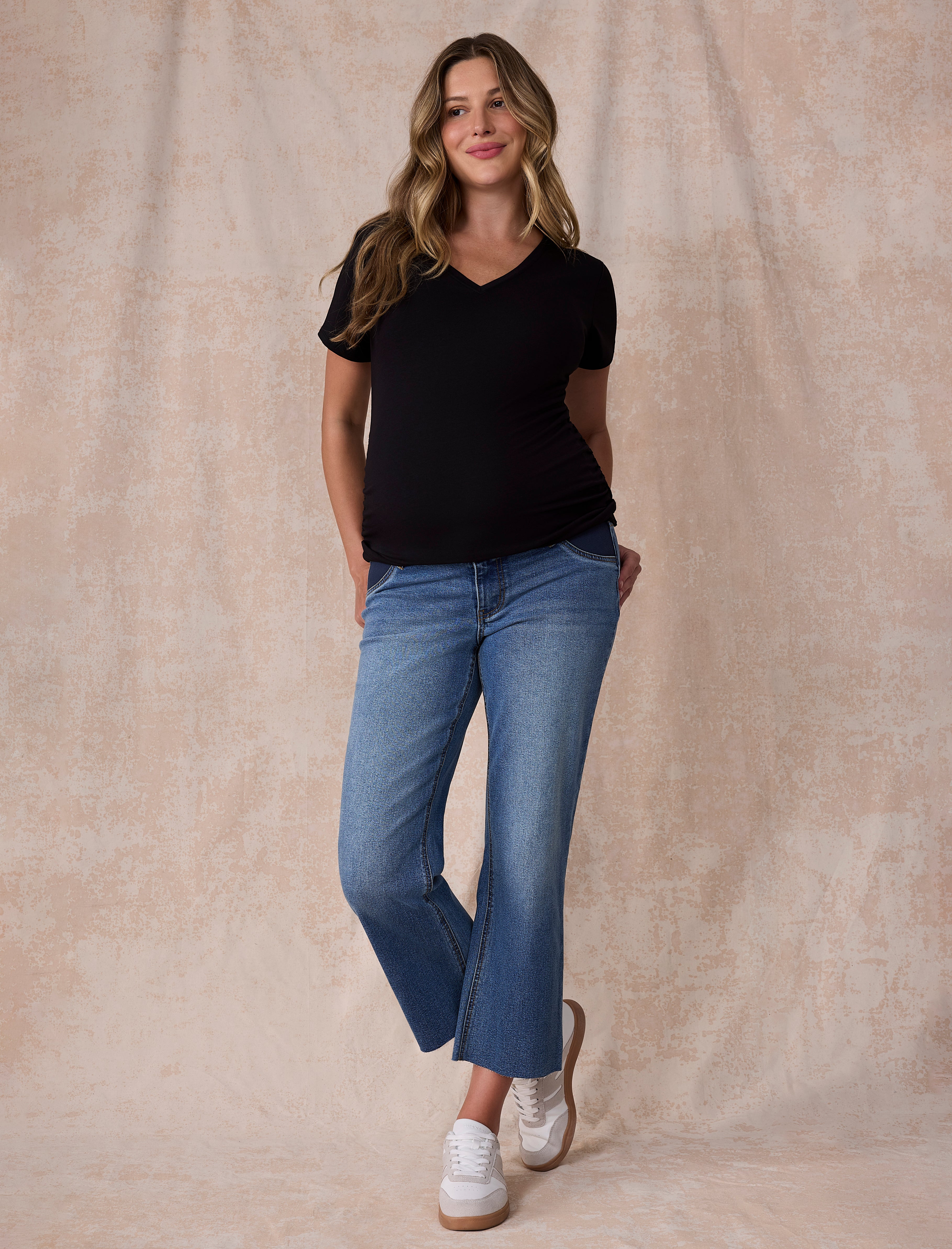 Pregnant woman wearing maternity blue jeans and black t-shirt on a light gray background