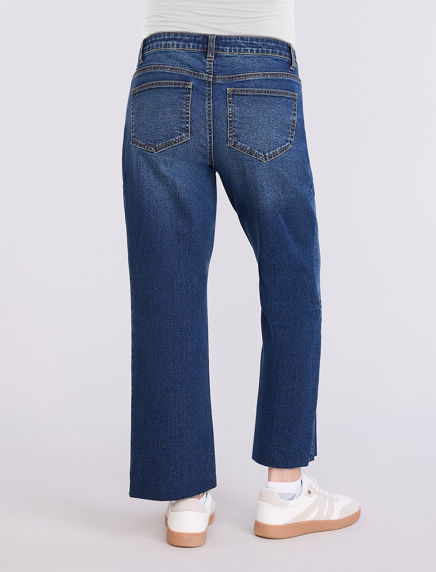 Person wearing maternity blue jeans and white sneakers on a light gray background