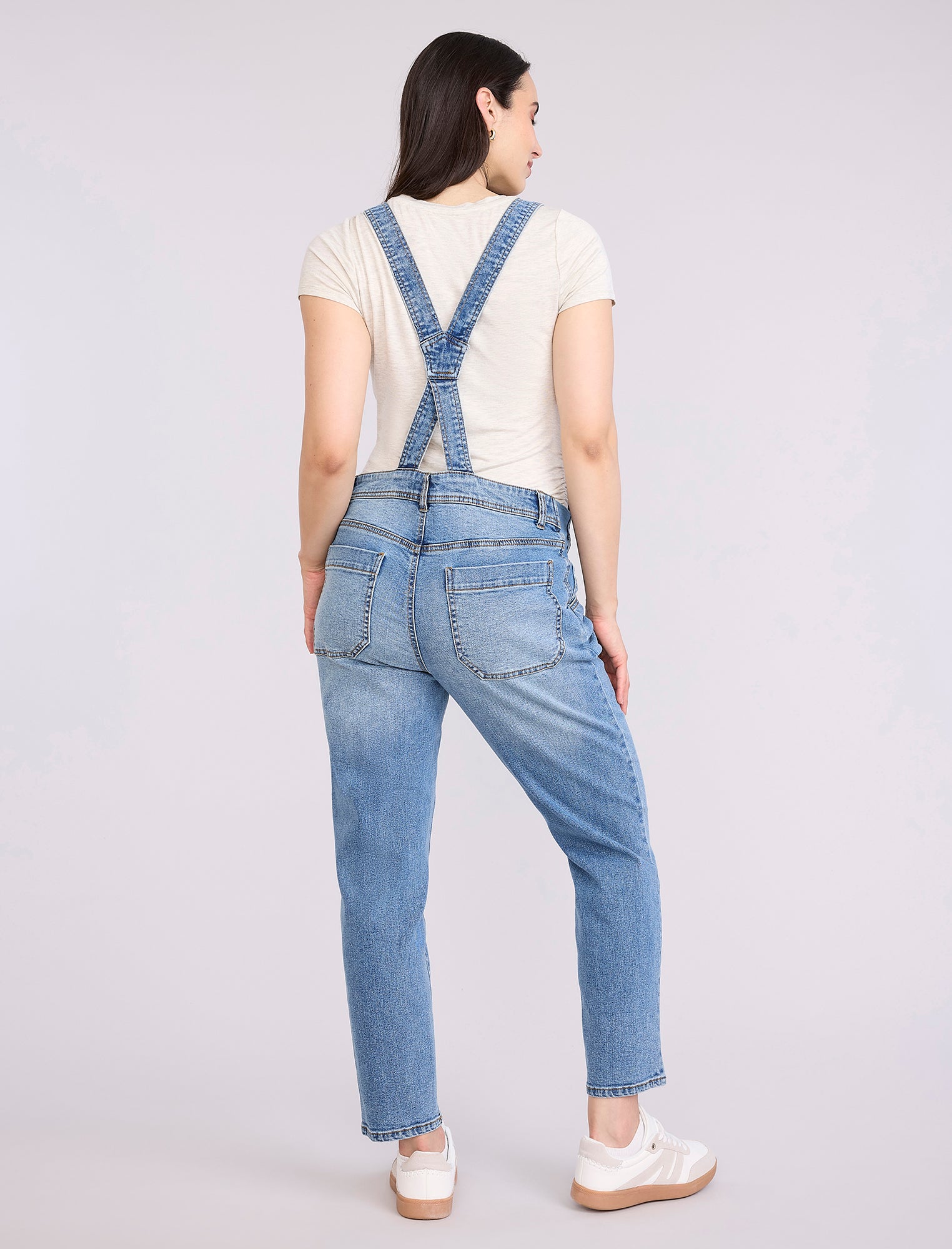 Pregnant woman wearing a denim overalls on a plain background
