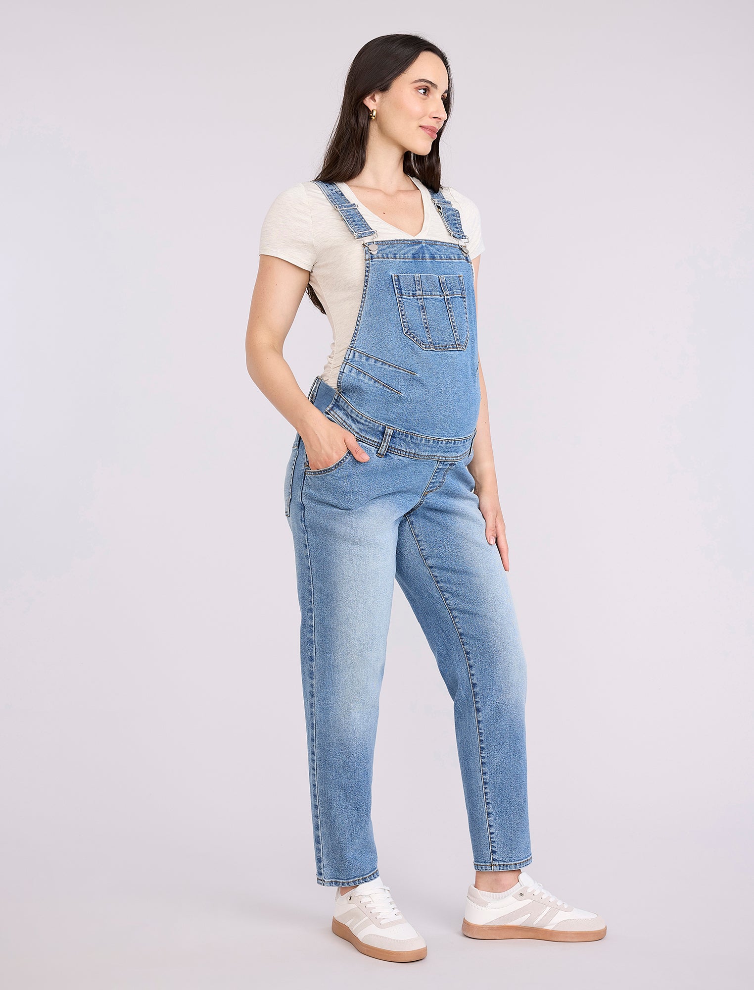 Pregnant woman wearing a denim overalls on a plain background