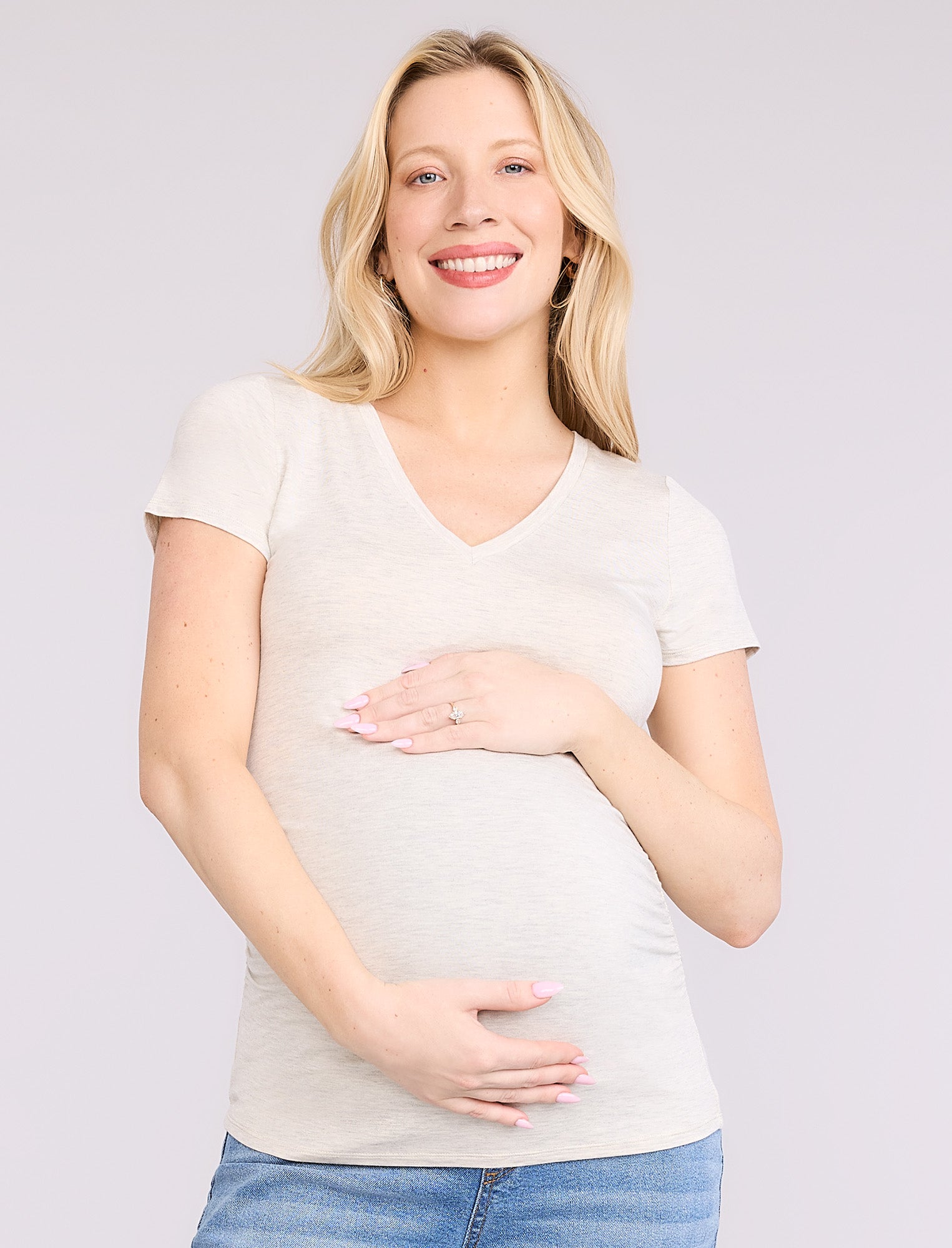 Pregnant woman wearing an off-white t-shirt and blue jeans on a plain background