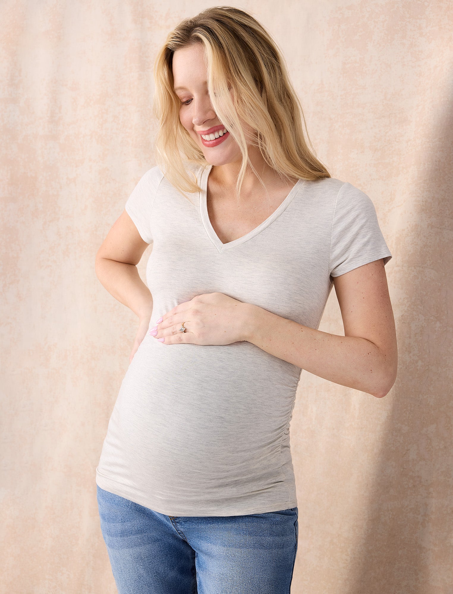 Pregnant woman wearing an off-white t-shirt and blue jeans on a plain background