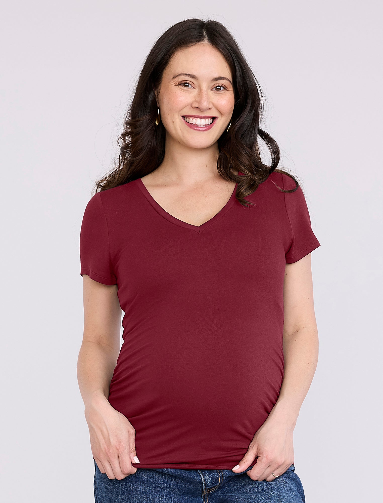 Pregnant woman wearing a maroon t-shirt against a plain background