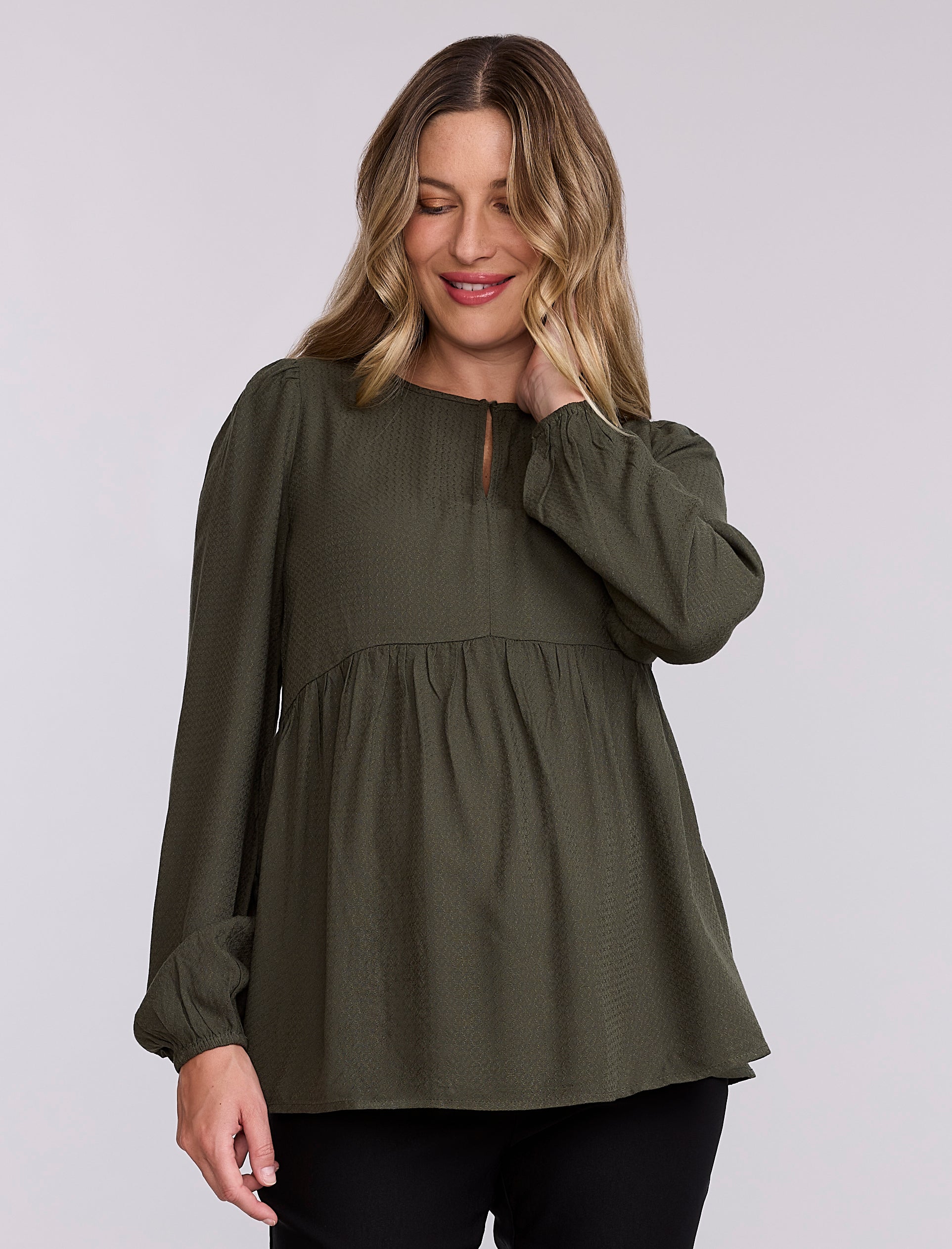 Pregnant woman wearing an olive green long-sleeve top against a plain background