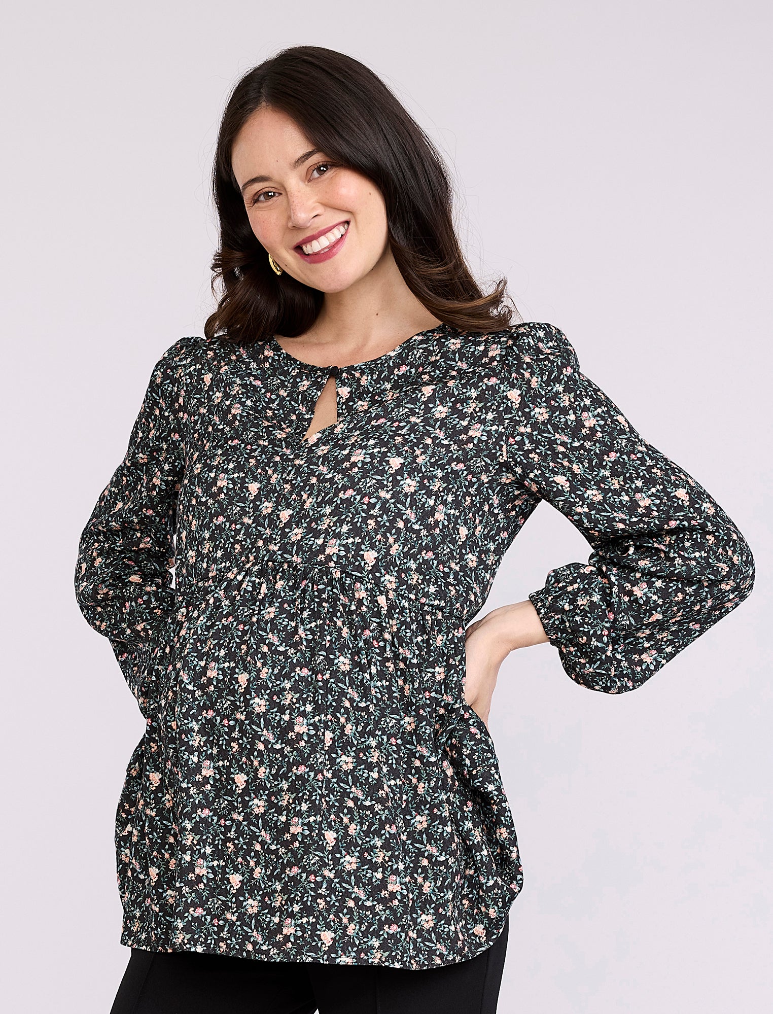 Pregnant woman wearing a black floral blouse against a plain background