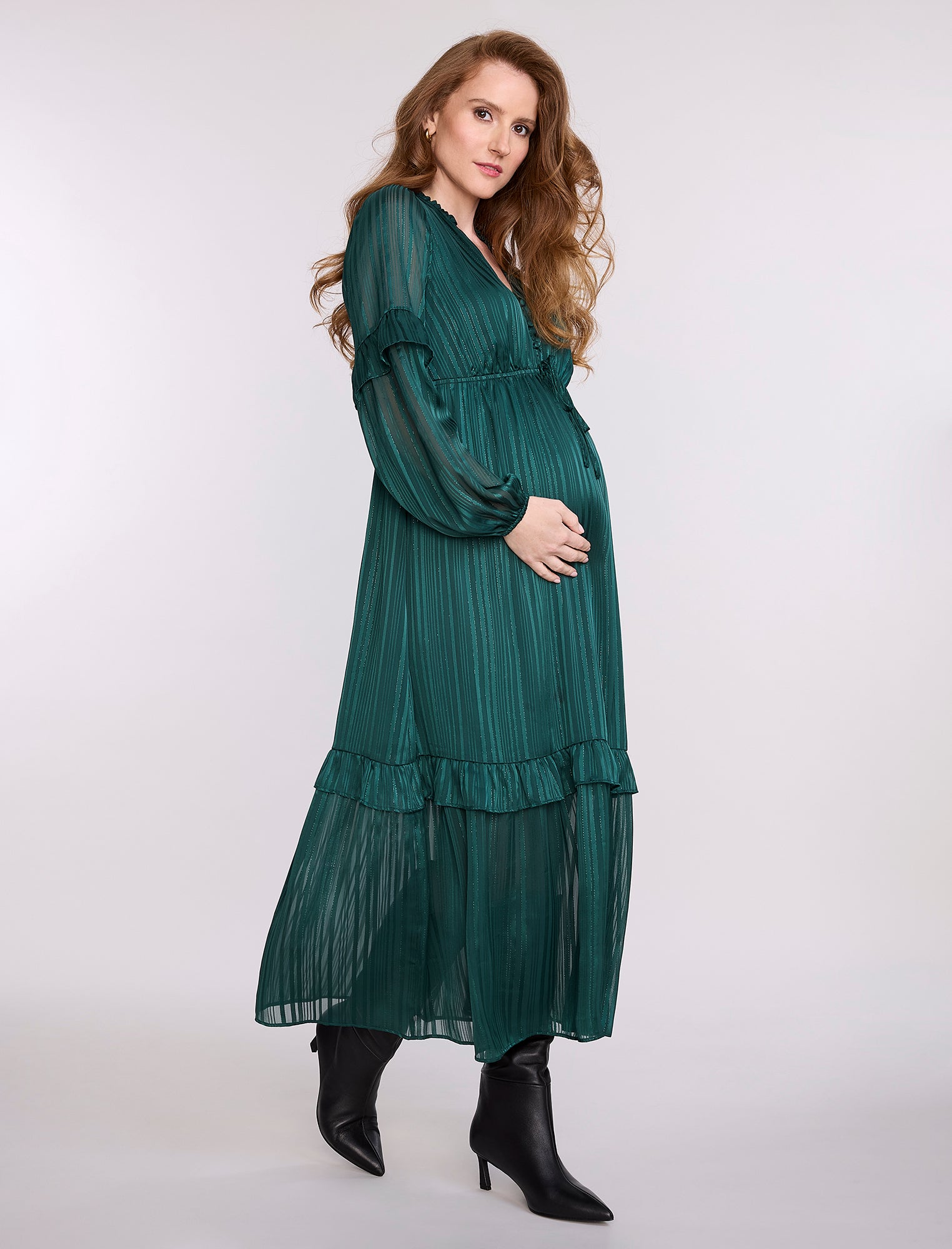Pregnant woman wearing a green dress with long sleeves and ruffled layers on a white background