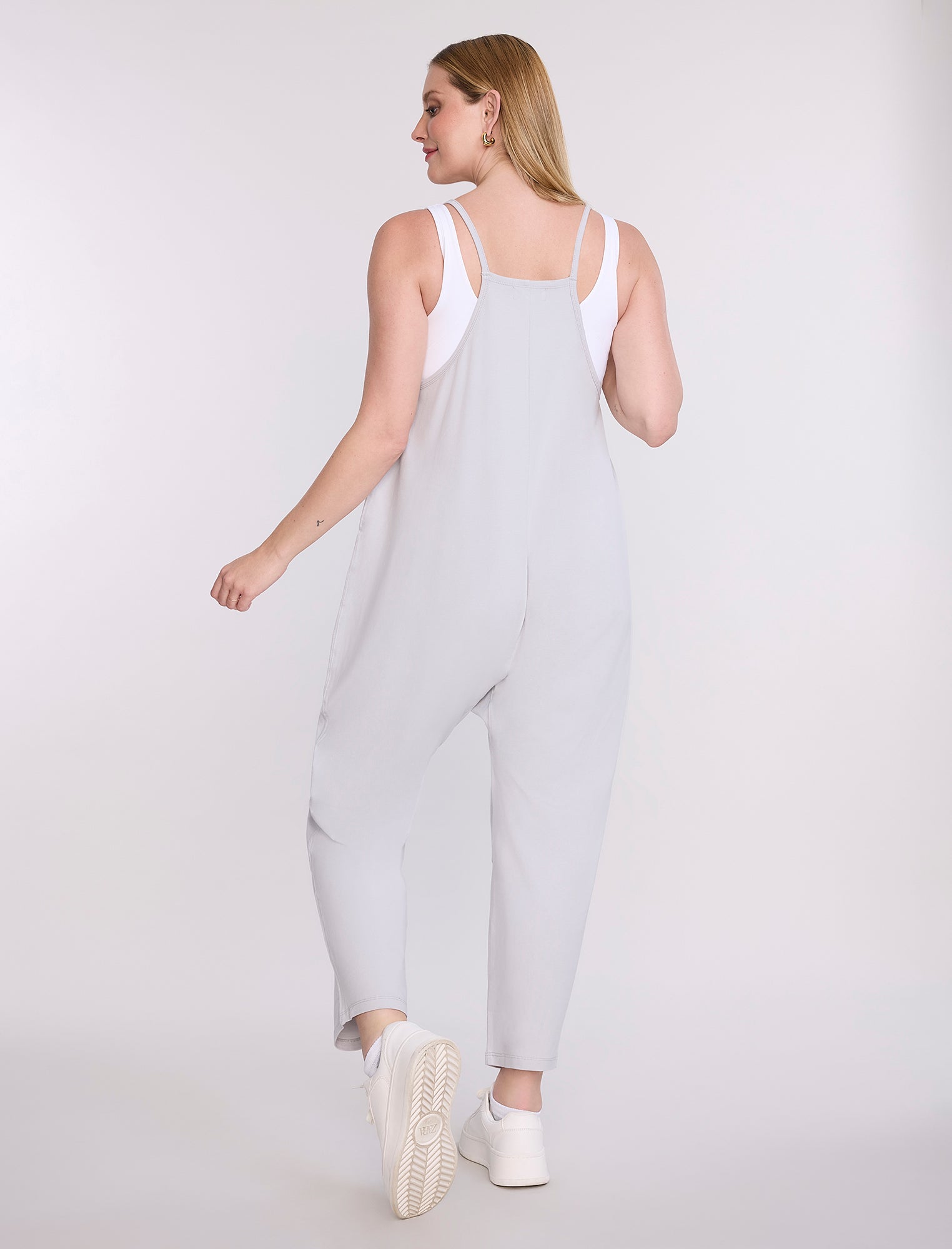 Pregnant woman wearing a light gray jumpsuit on a white background