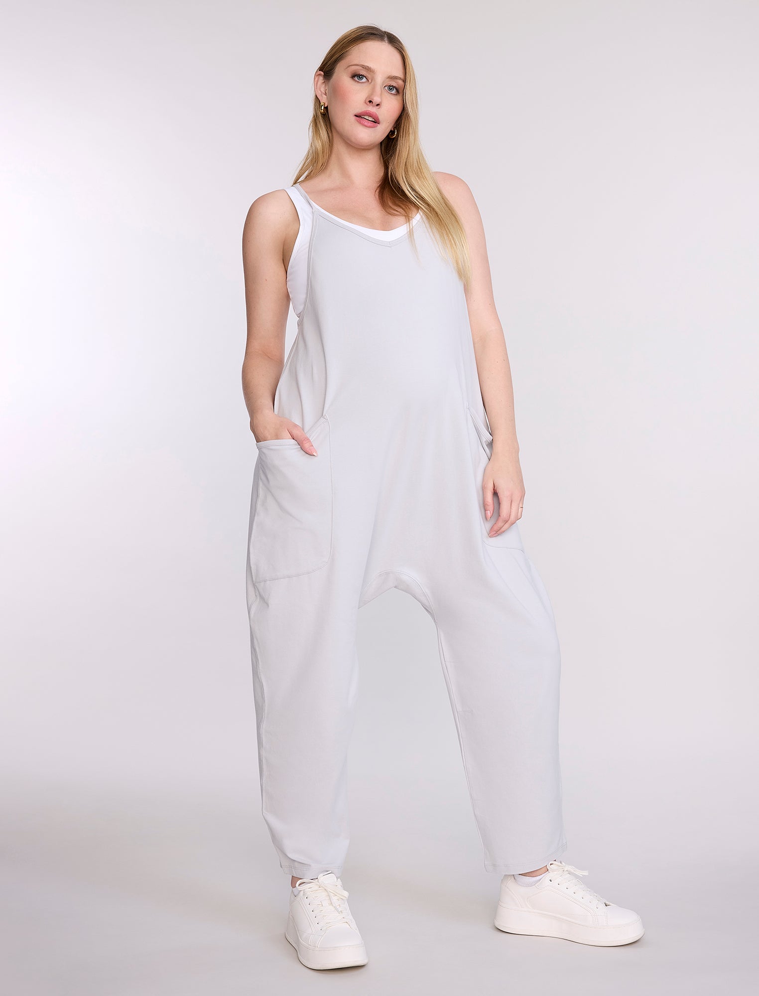 Pregnant woman wearing a light gray jumpsuit on a white background