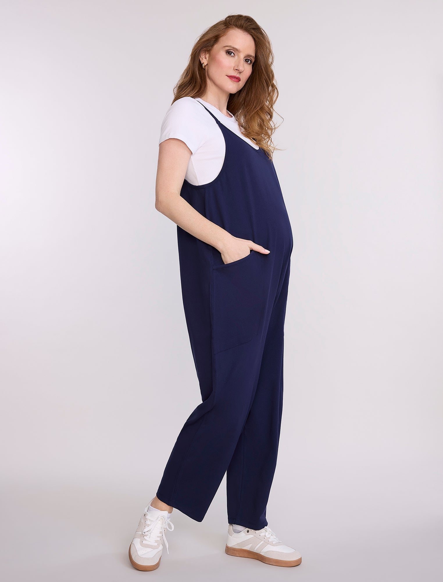 Pregnant woman wearing a navy blue jumpsuit over a white shirt on a light gray background