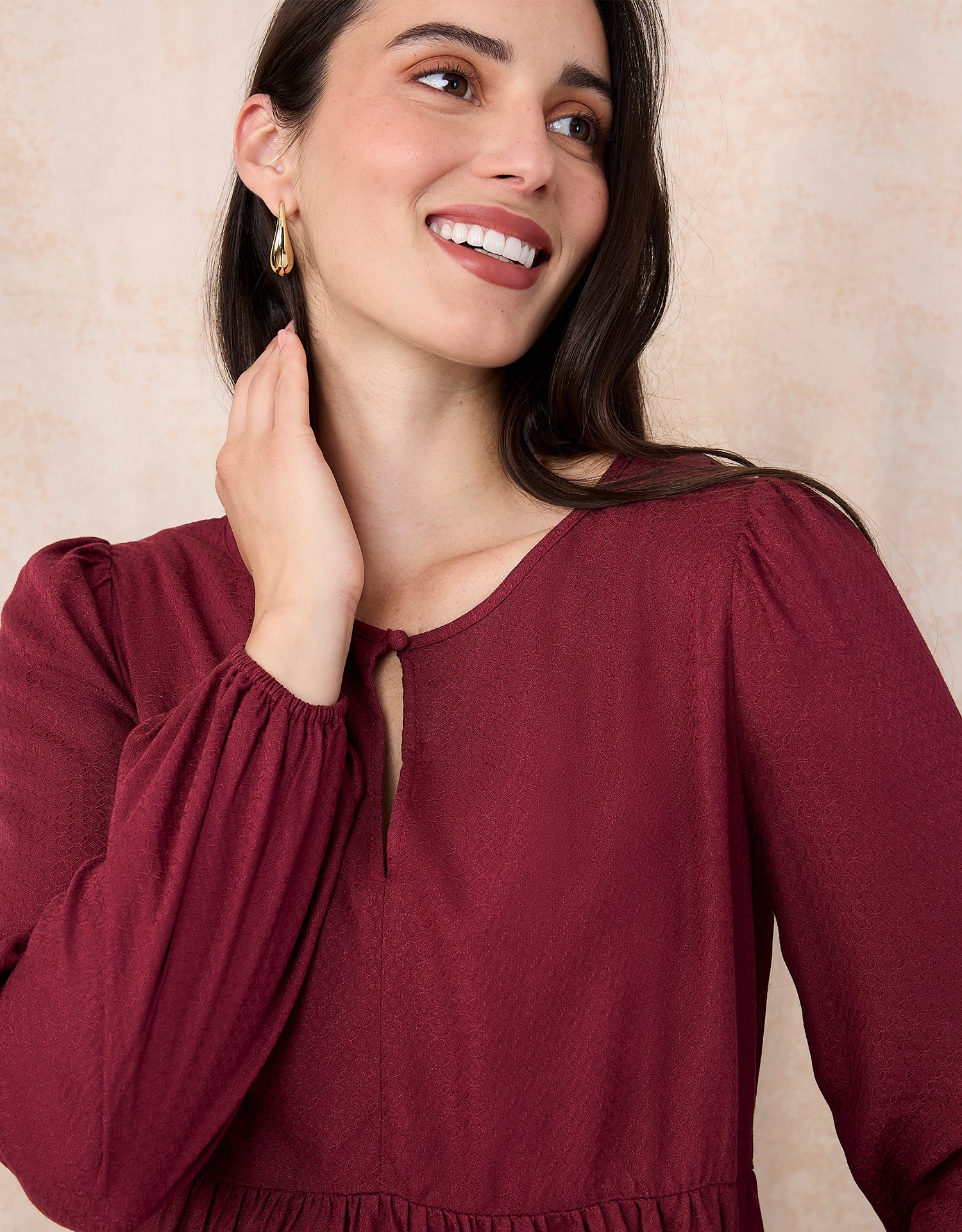 Woman wearing a burgundy top with long sleeves against a beige background