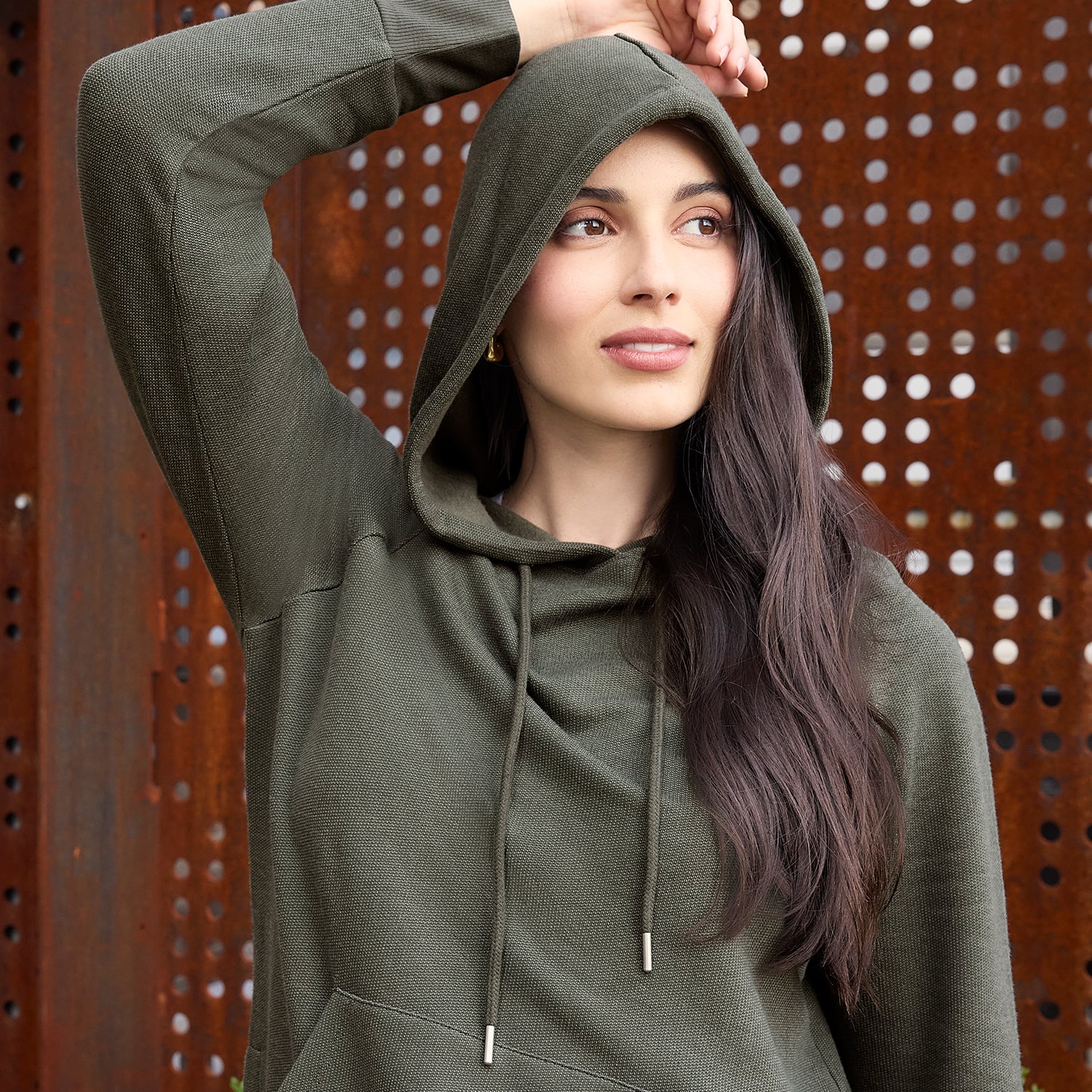 Woman wearing a green hoodie against a perforated metal background