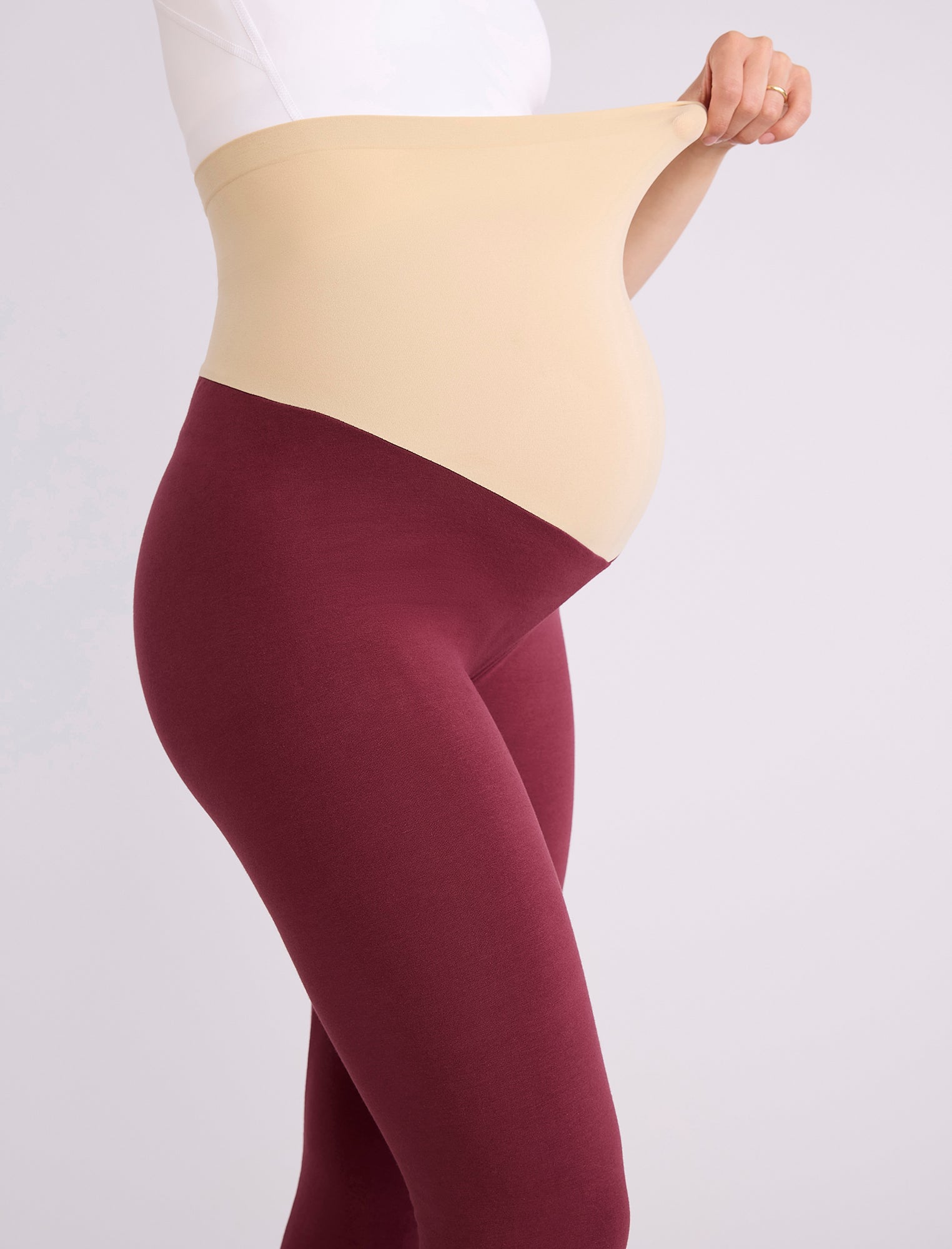 Maroon leggings worn by a pregnant woman on a white background