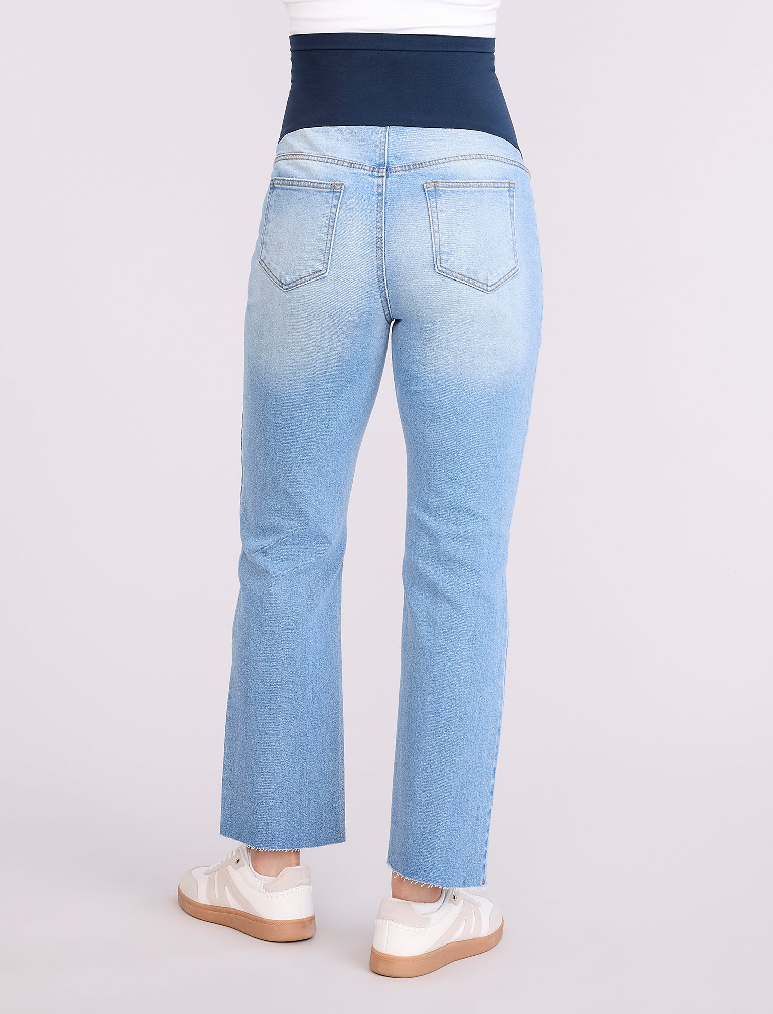 Pregnant woman wearing light blue jeans on a neutral background