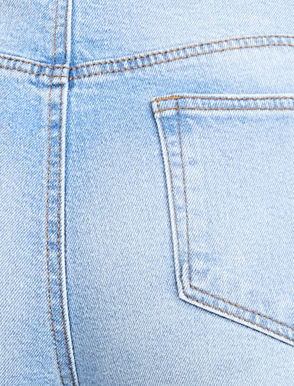 Pregnant woman wearing light blue jeans on a neutral background