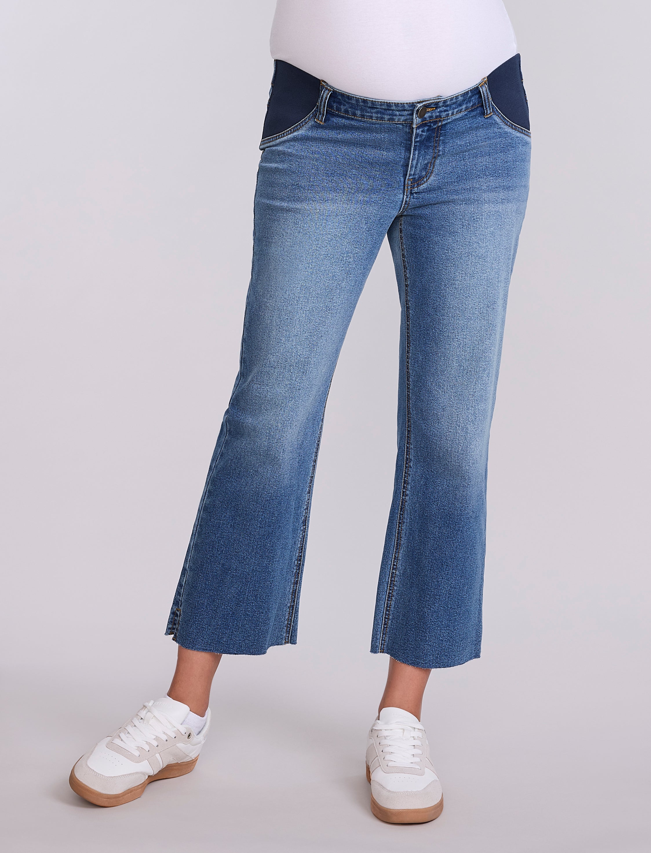 Person wearing maternity blue jeans and white sneakers on a light gray background