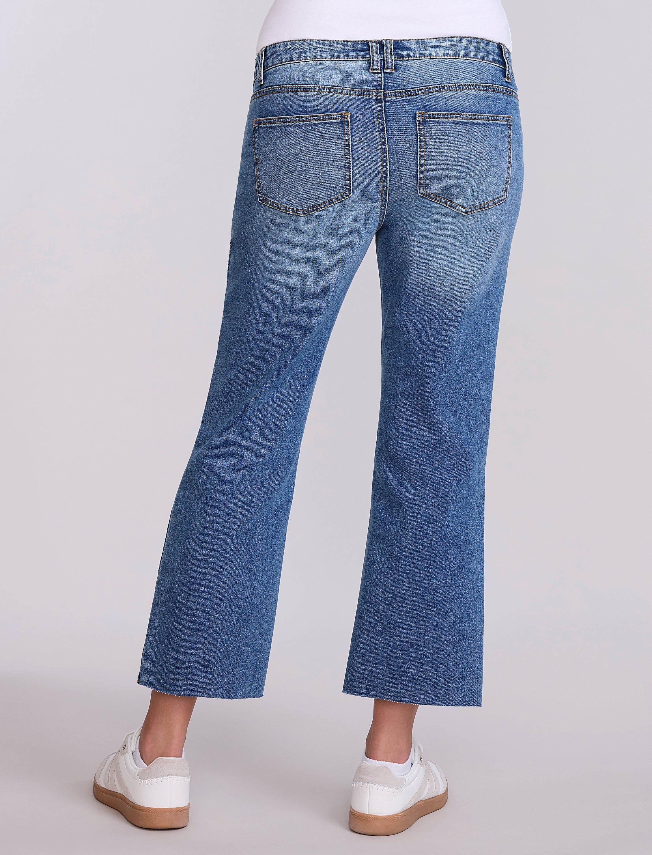 Person wearing maternity blue jeans and white sneakers on a light gray background