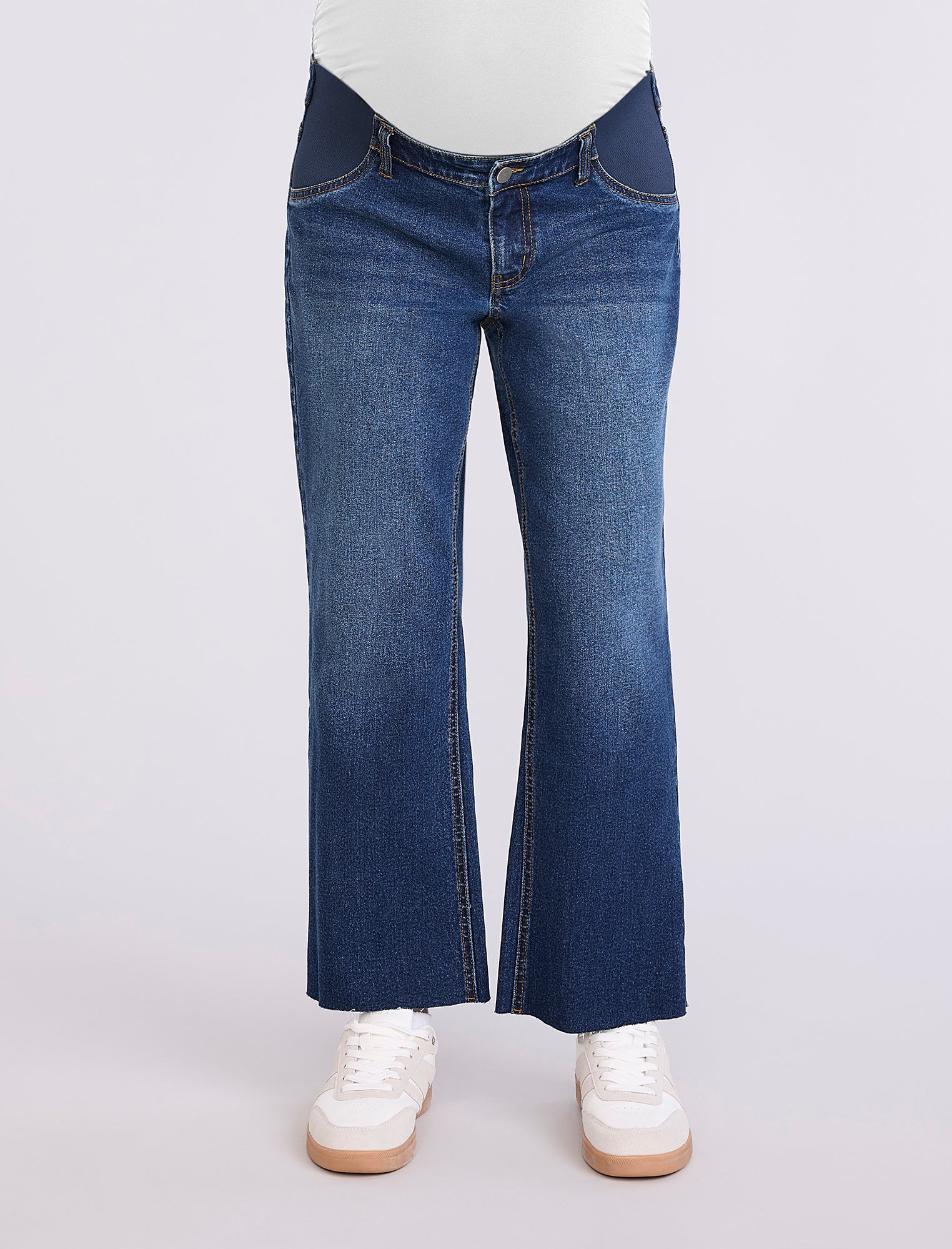 Person wearing maternity blue jeans and white sneakers on a light gray background