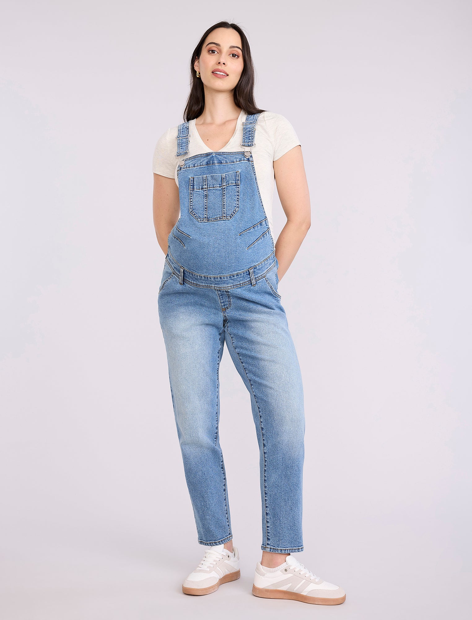 Pregnant woman wearing a denim overalls on a plain background