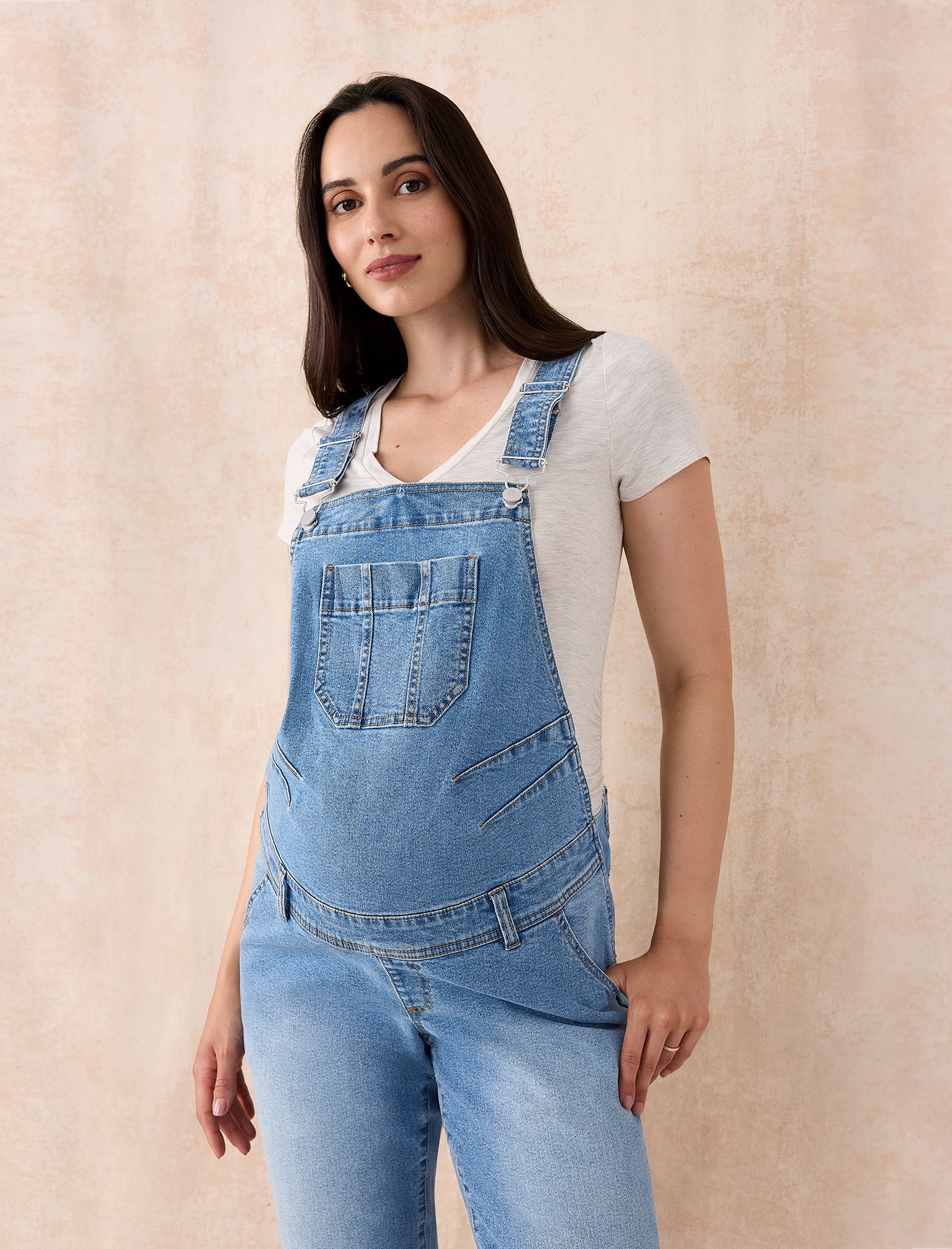 Pregnant woman wearing a denim overalls on a plain background