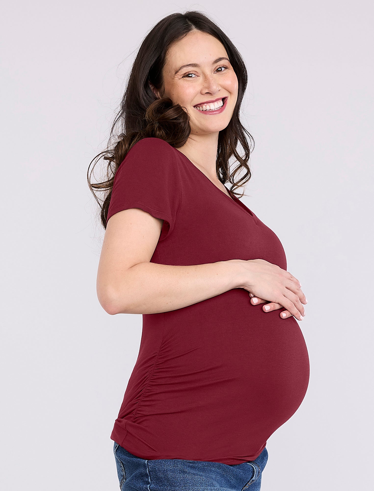 Pregnant woman wearing a maroon t-shirt against a plain background