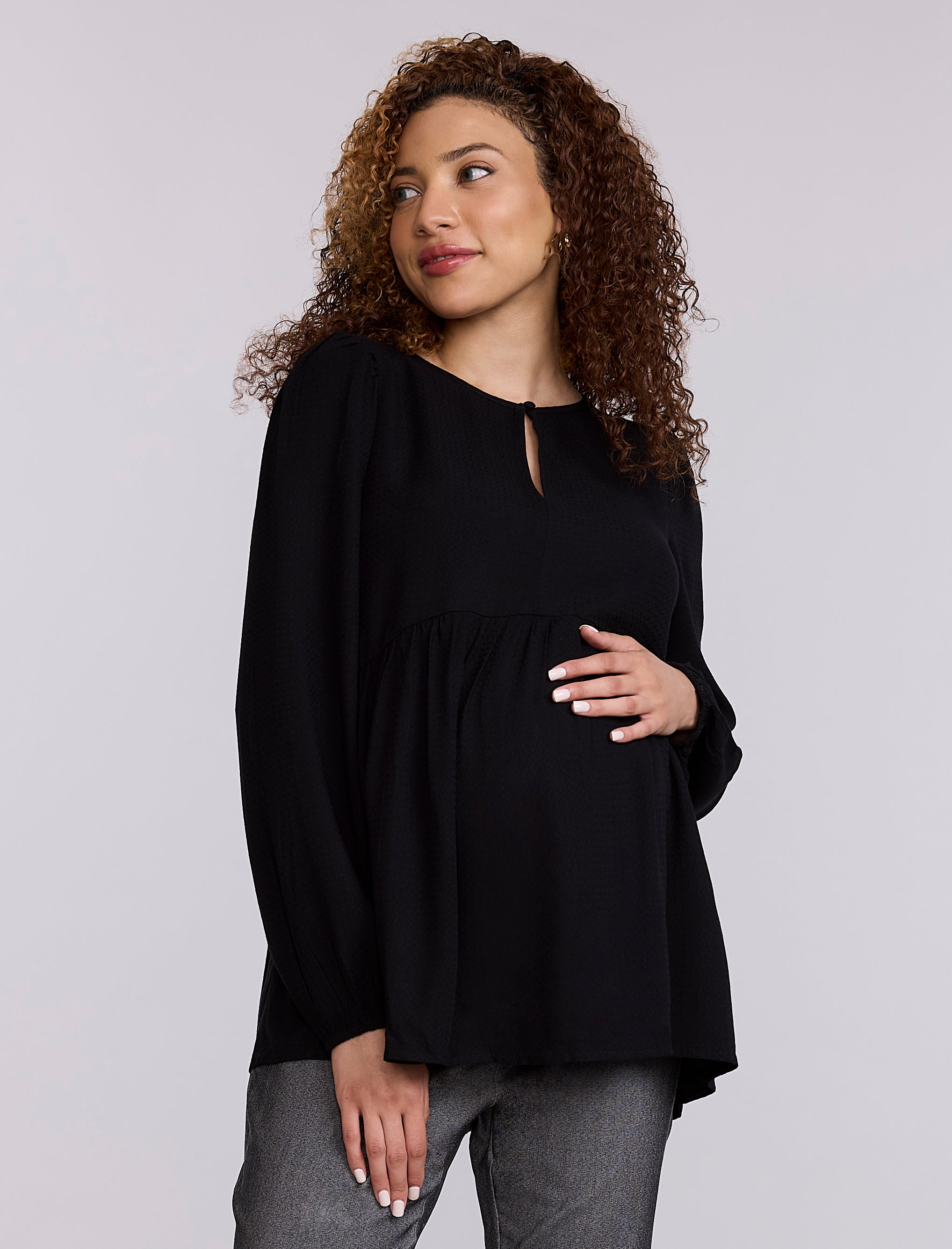 Pregnant woman wearing a black top and gray pants against a plain background