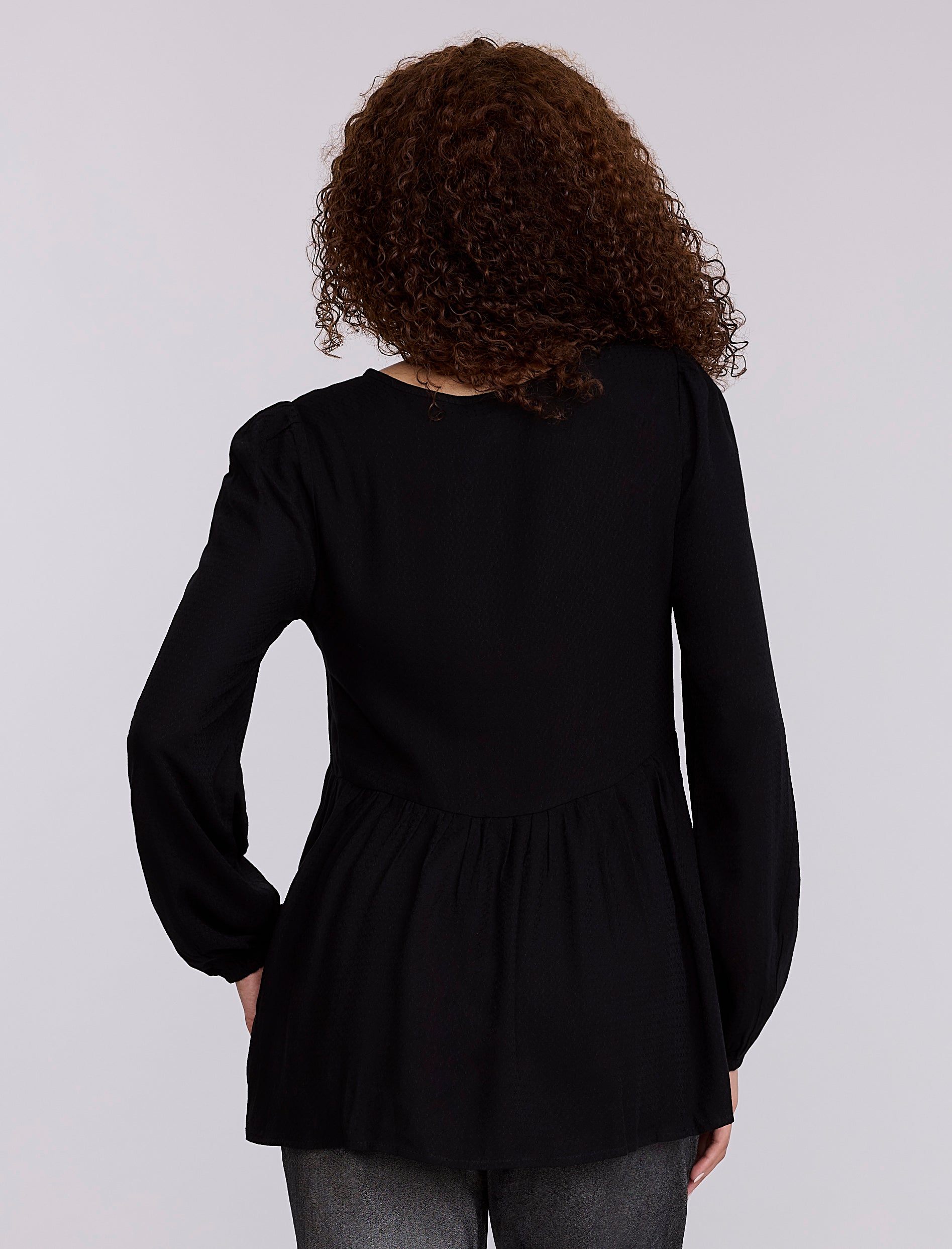 Pregnant woman wearing a black top and gray pants against a plain background