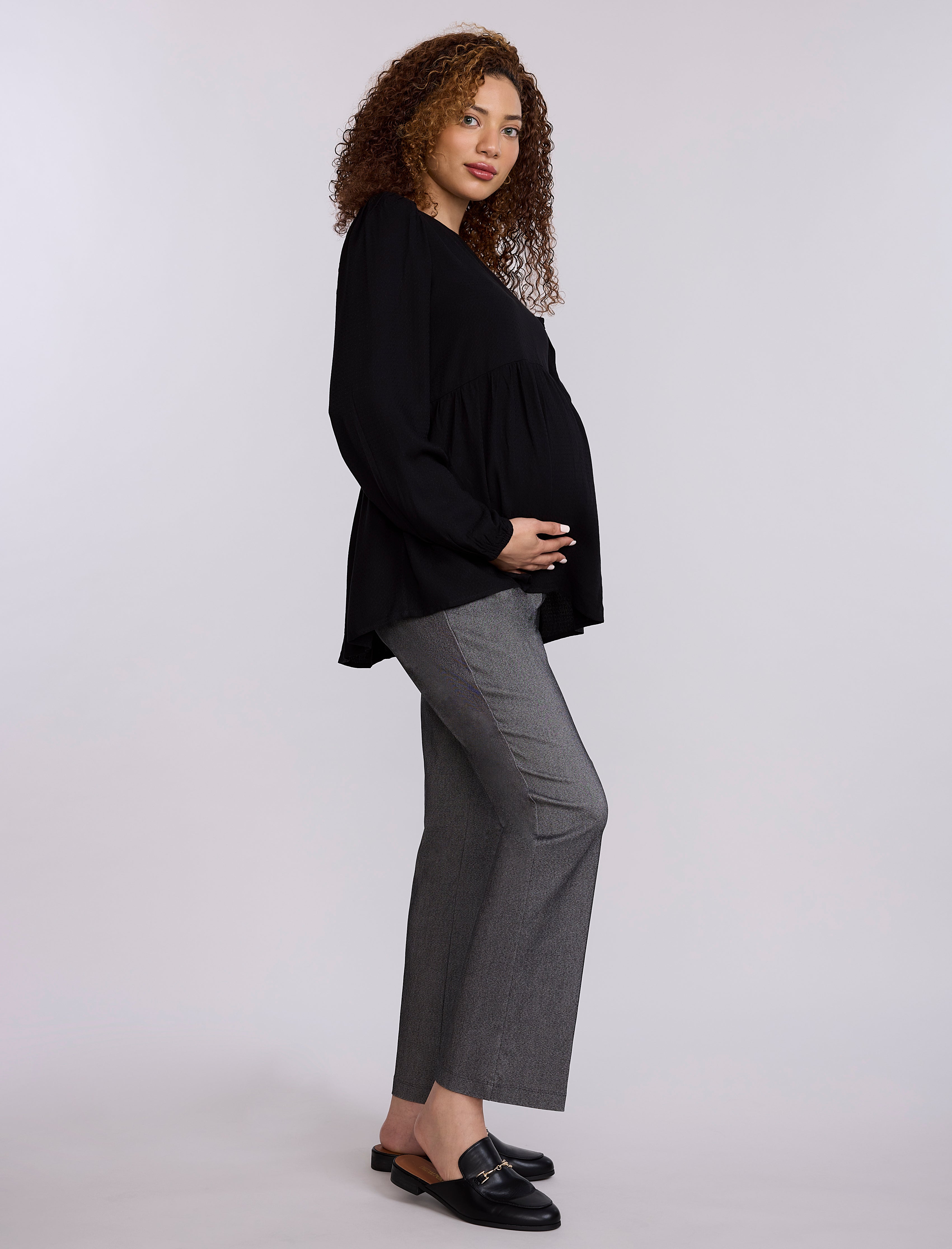 Pregnant woman wearing a black top and gray pants against a plain background