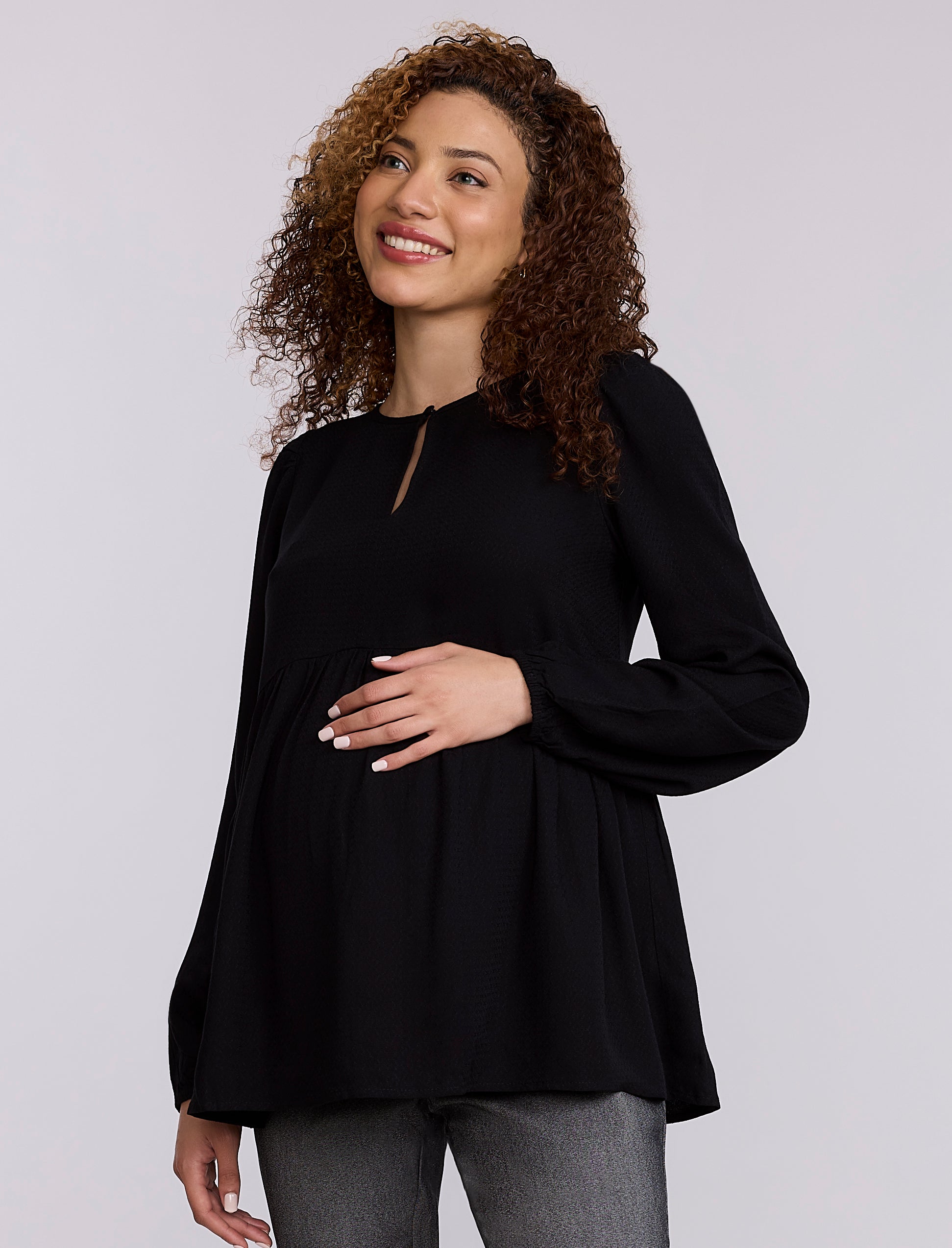 Pregnant woman wearing a black top and gray pants against a plain background