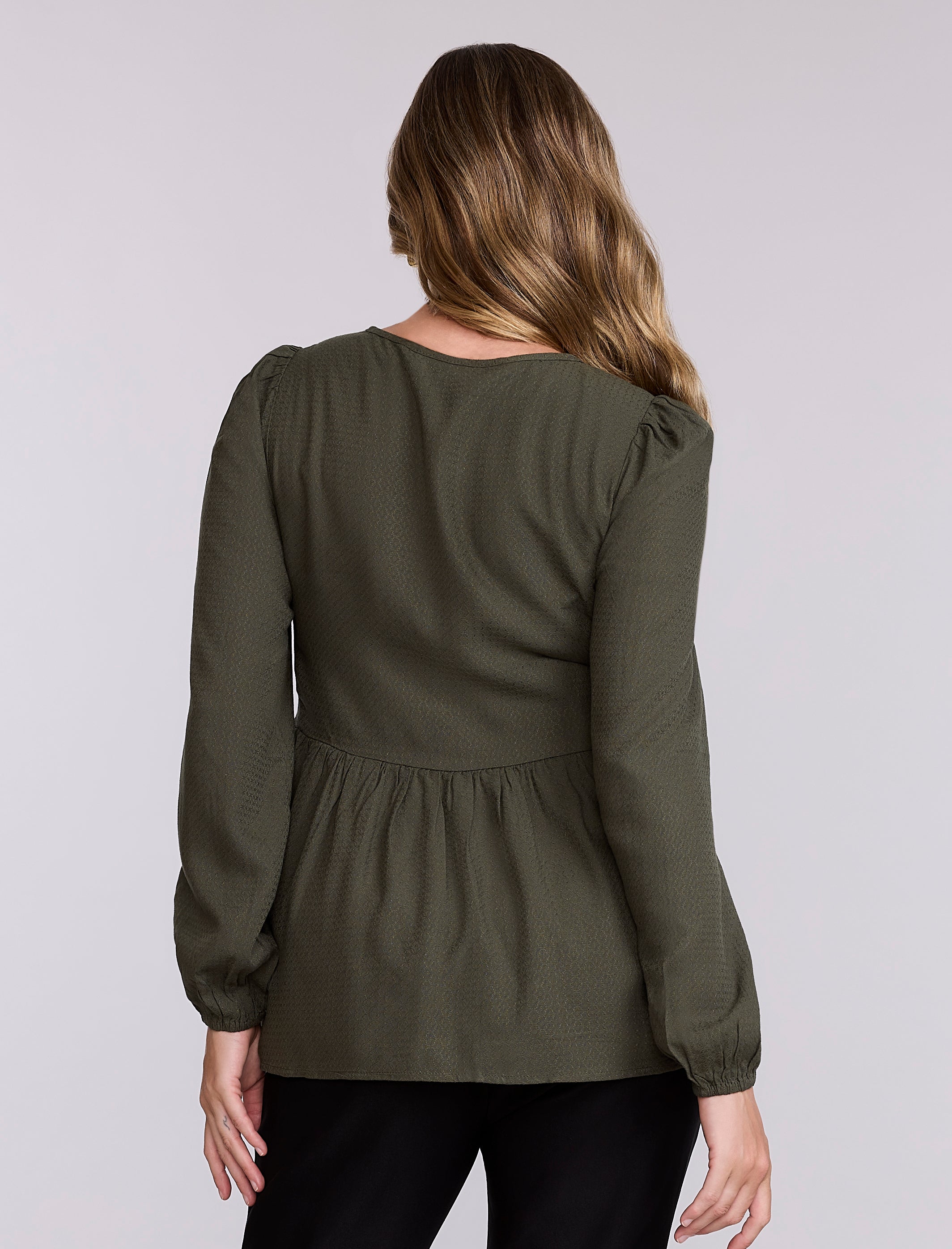 Pregnant woman wearing an olive green long-sleeve top against a plain background