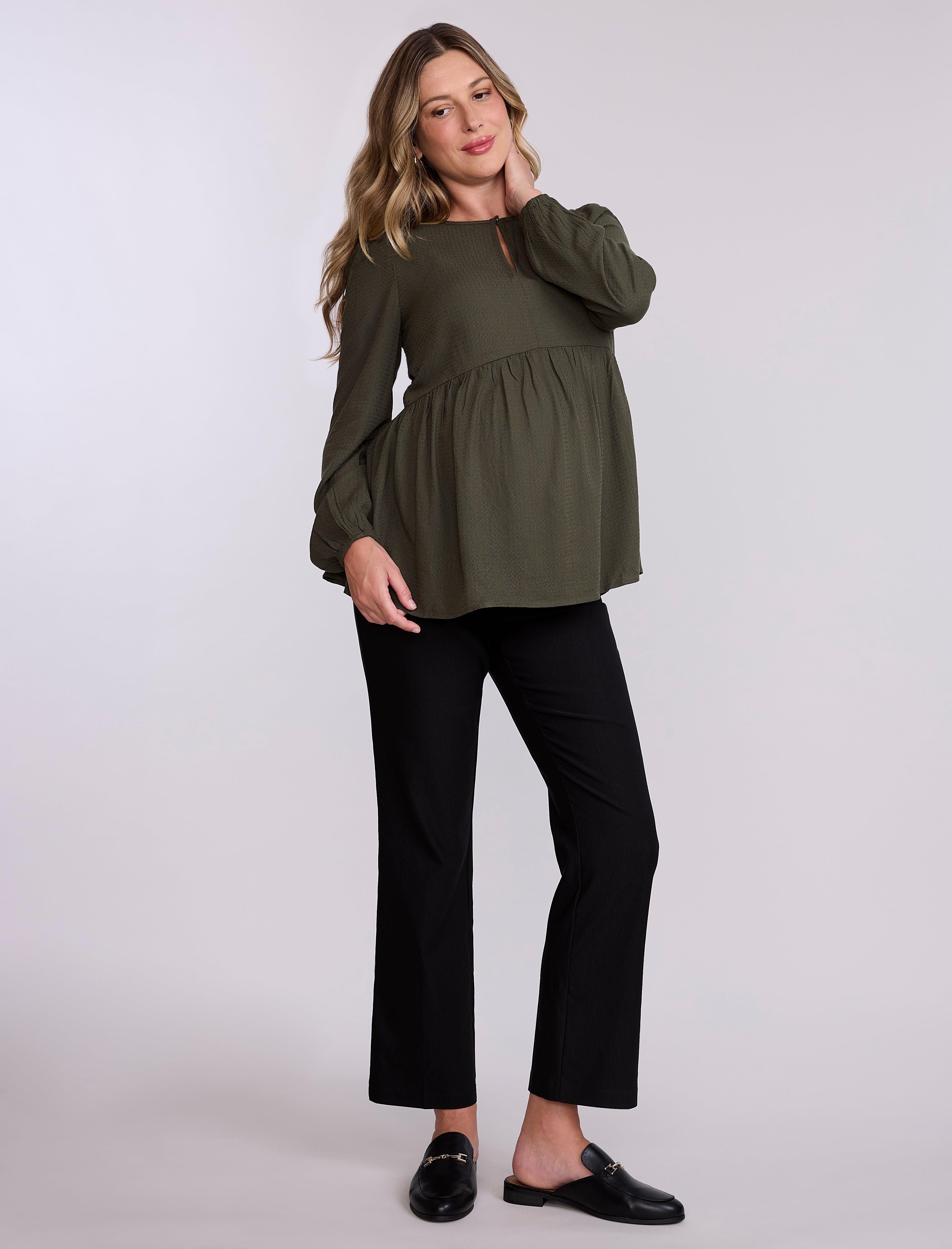 Pregnant woman wearing an olive green long-sleeve top against a plain background