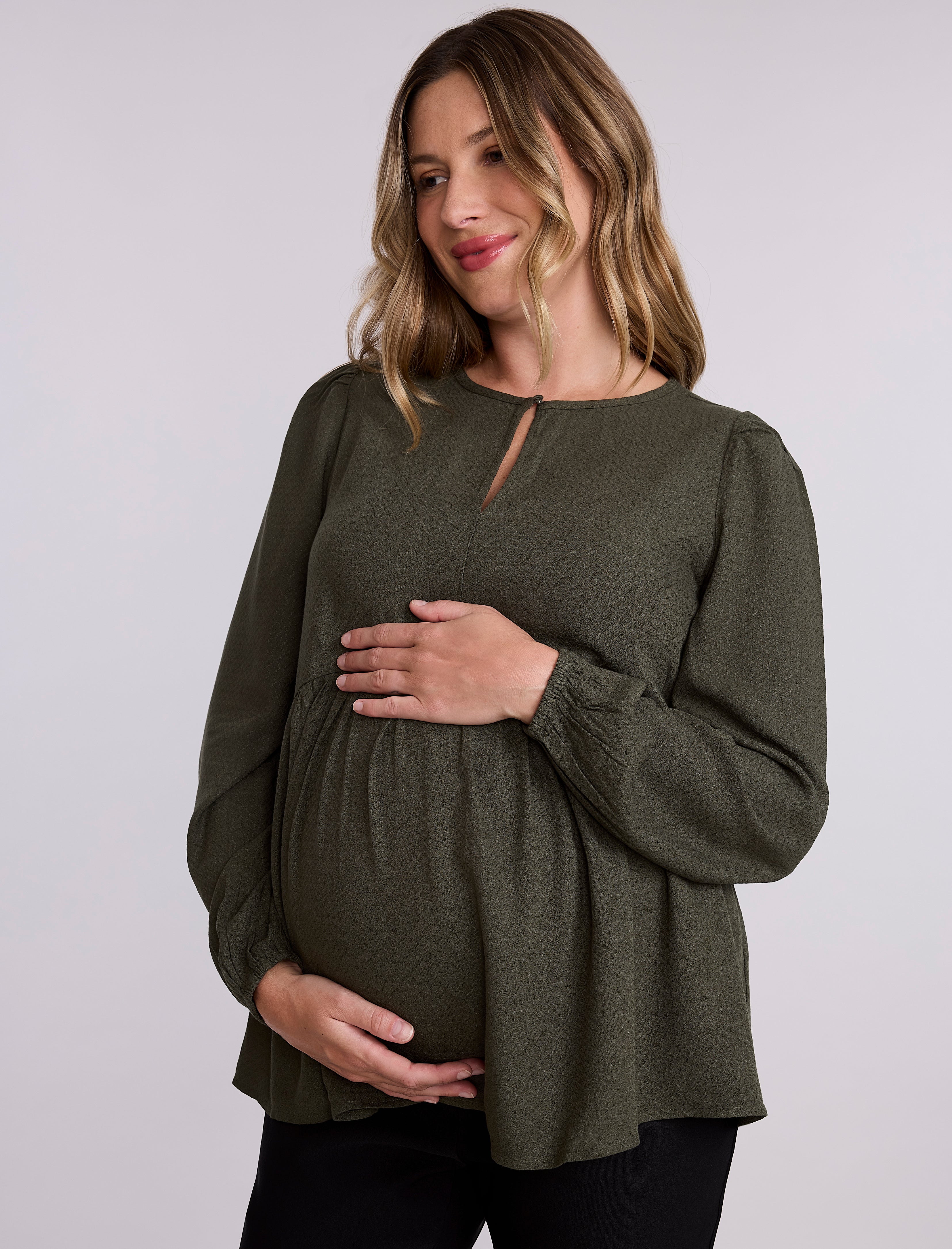 Pregnant woman wearing an olive green long-sleeve top against a plain background