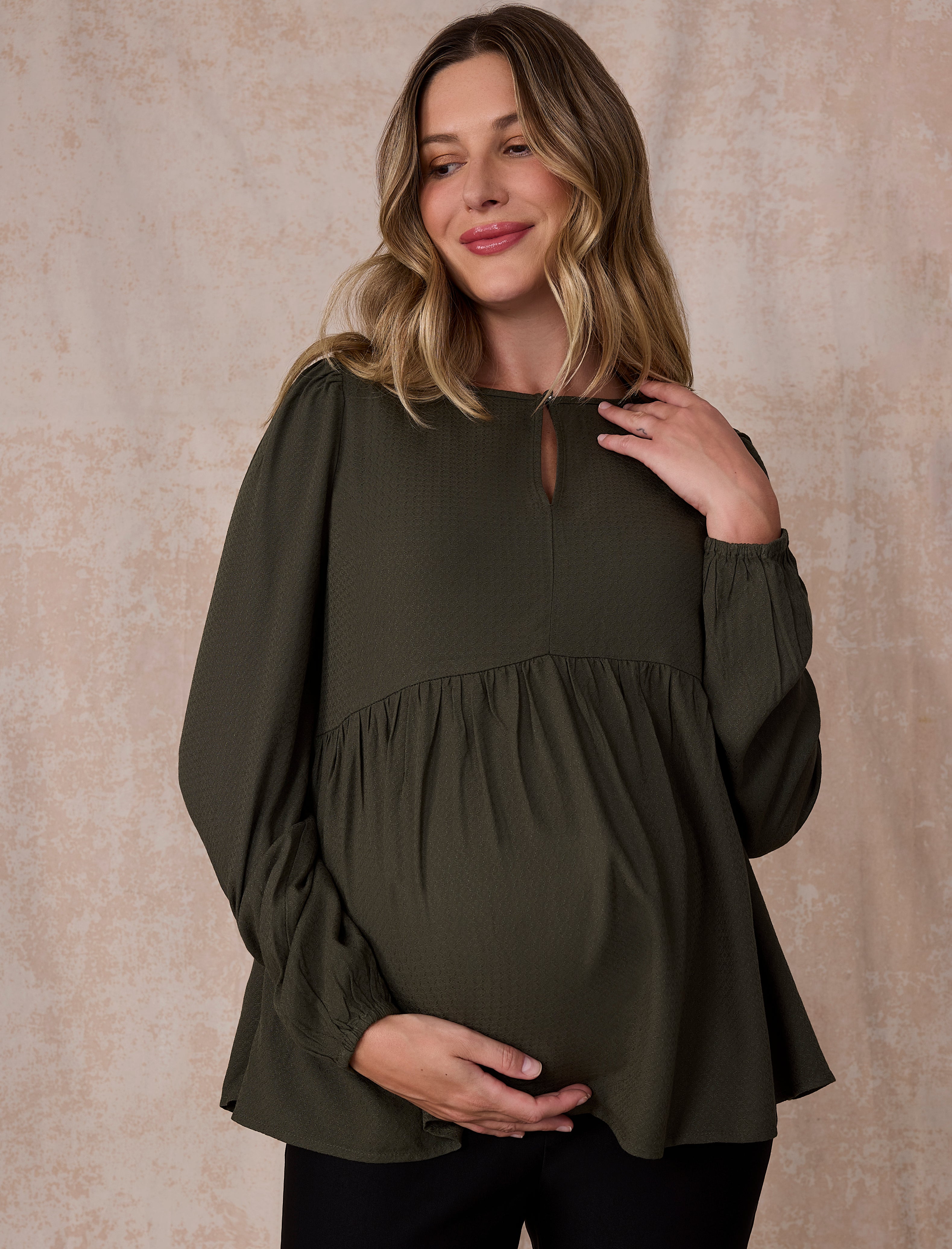 Pregnant woman wearing an olive green long-sleeve top against a plain background