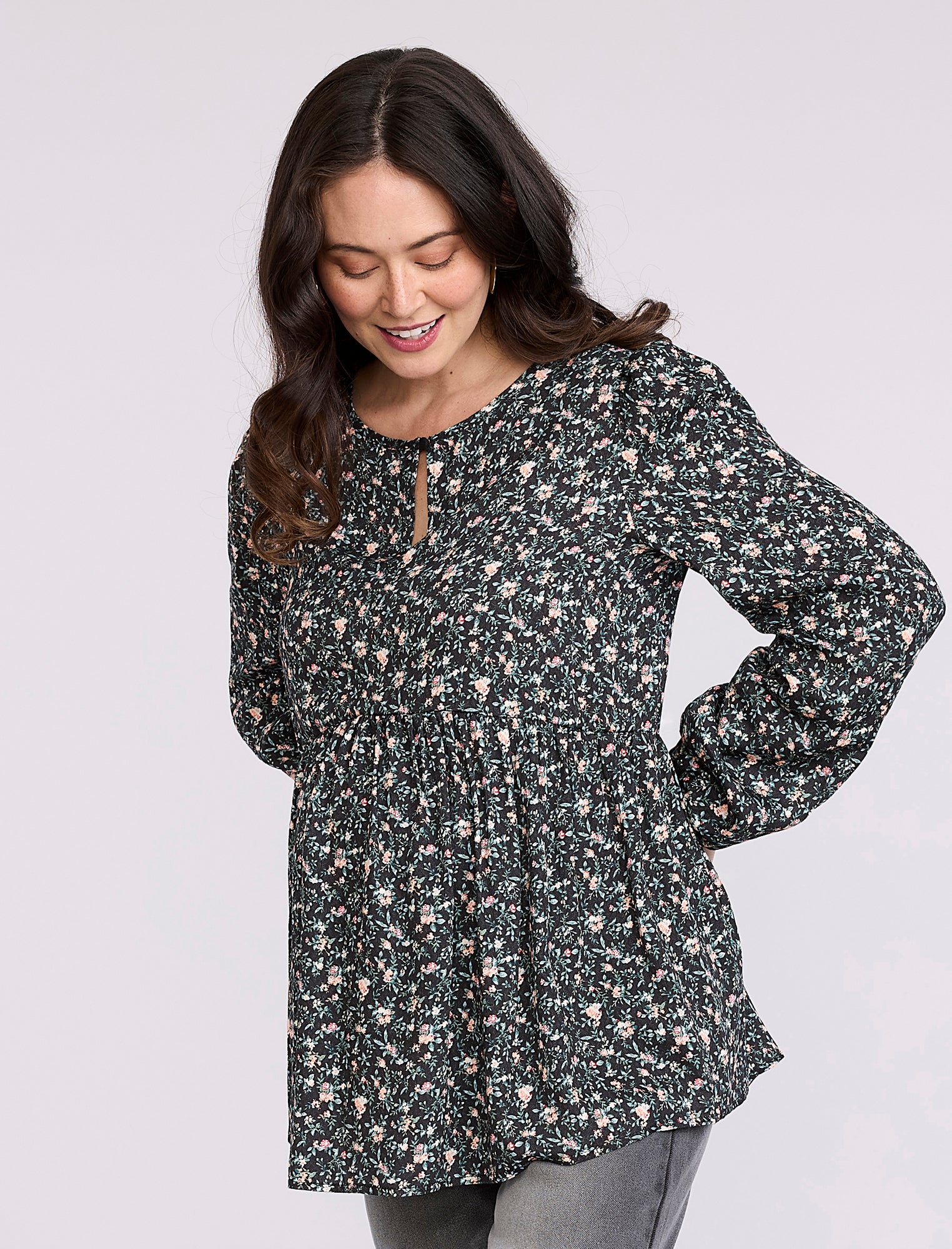 Pregnant woman wearing a black floral blouse against a plain background