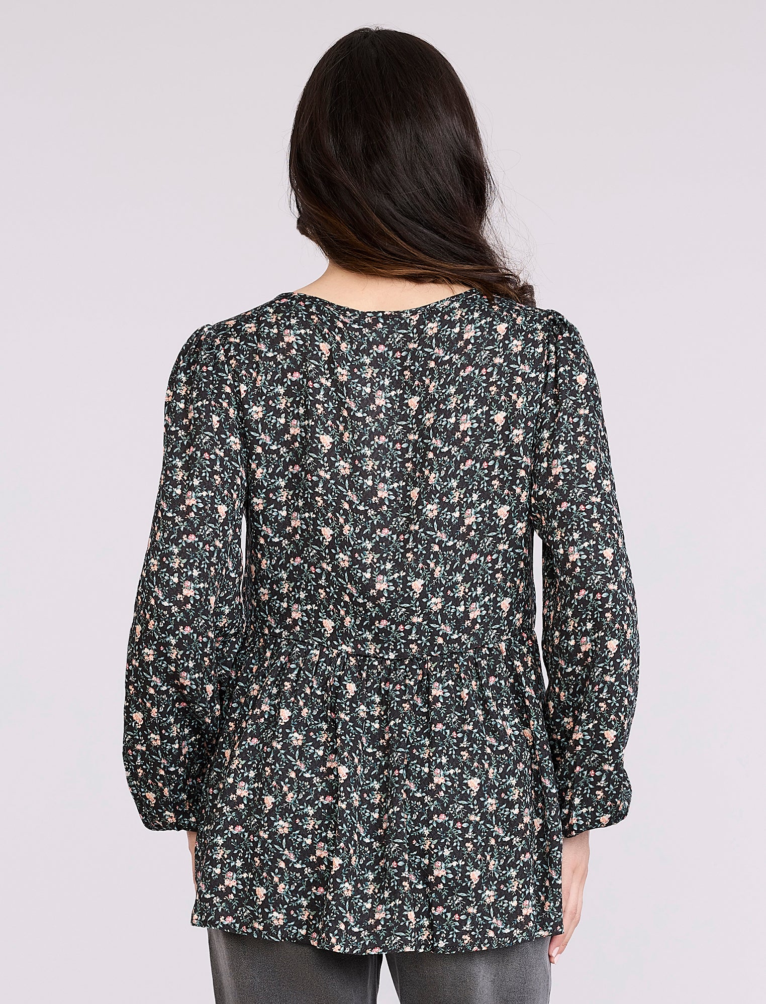 Pregnant woman wearing a black floral blouse against a plain background