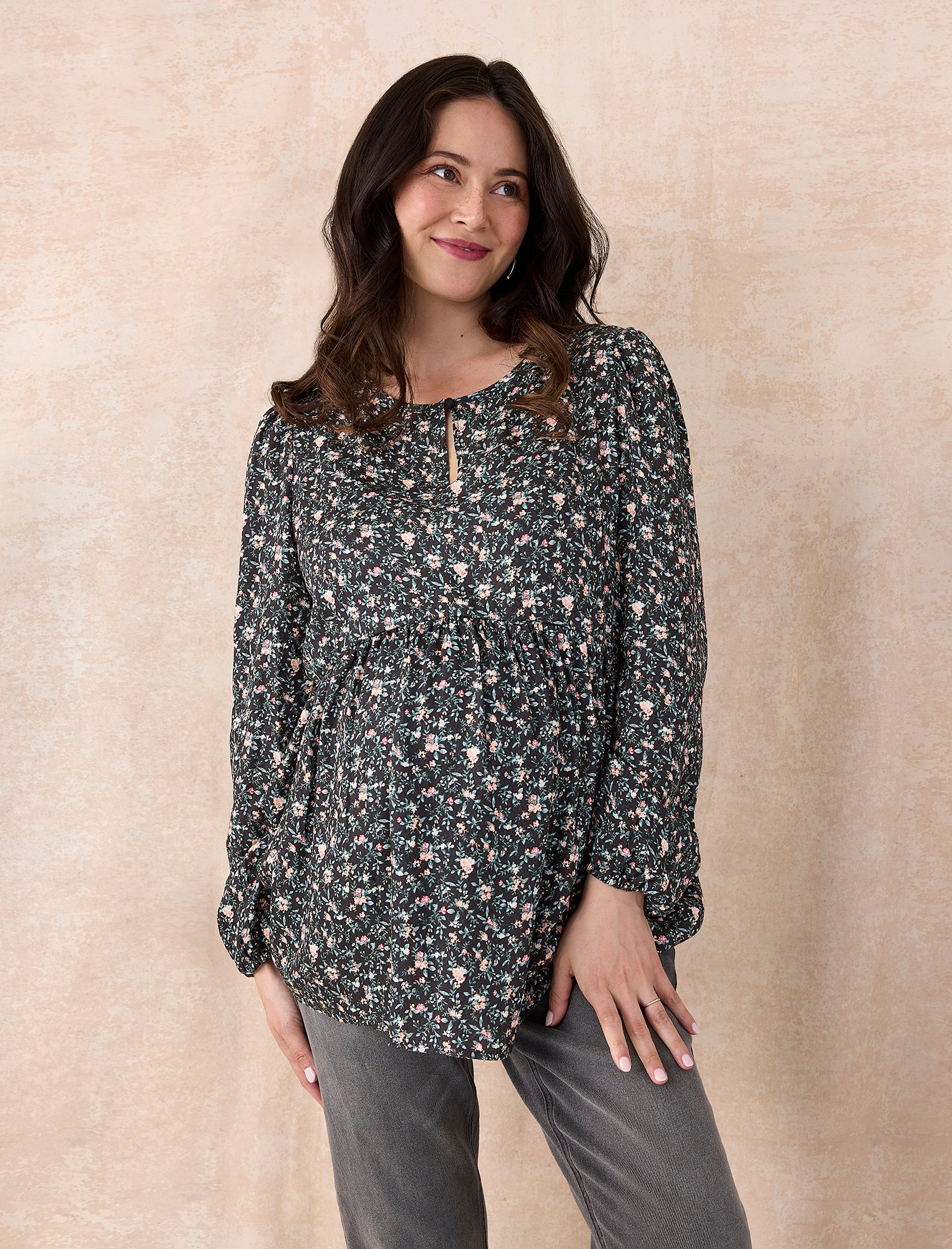Pregnant woman wearing a black floral blouse against a plain background
