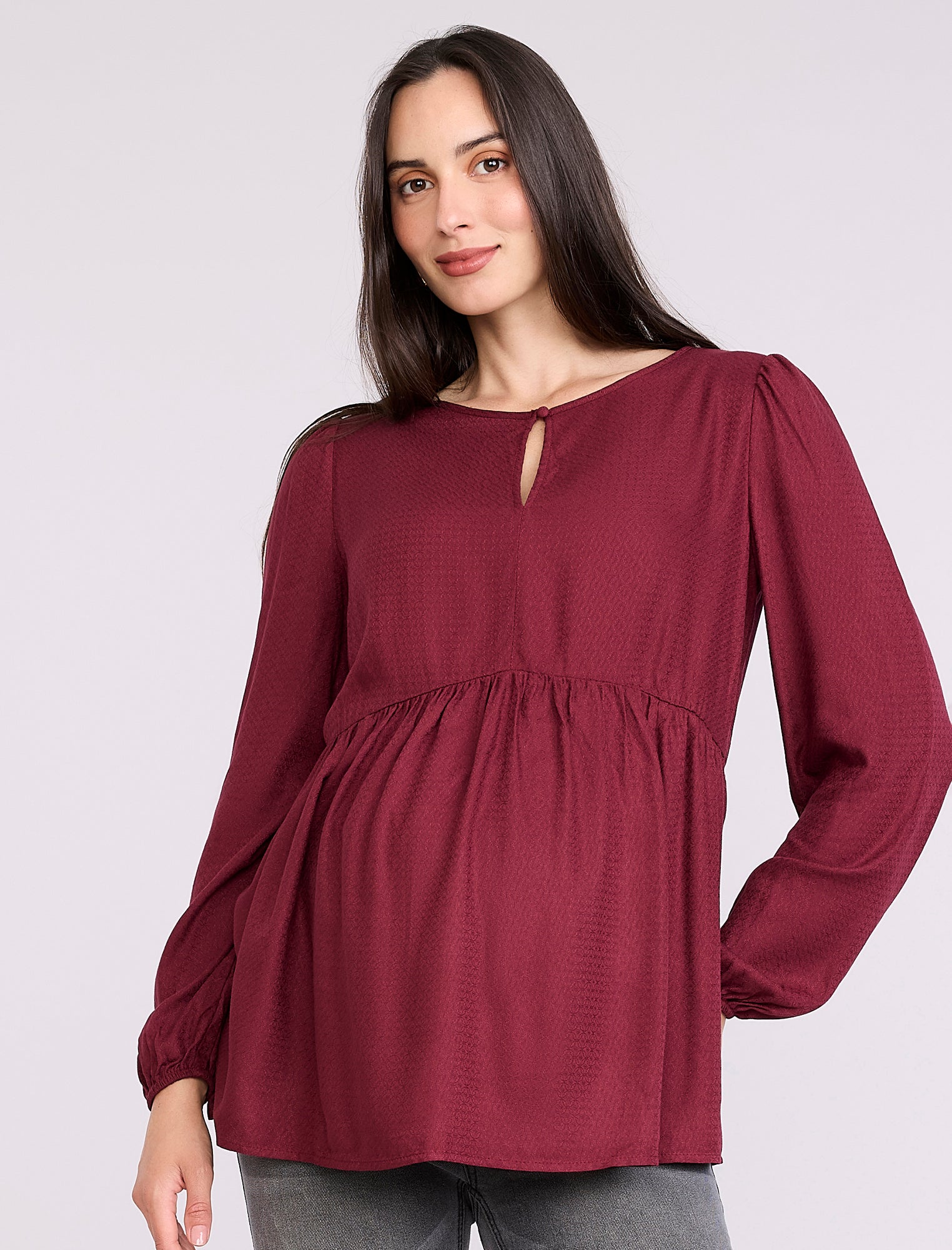 Pregnant woman wearing a burgundy long-sleeve top on a light gray background