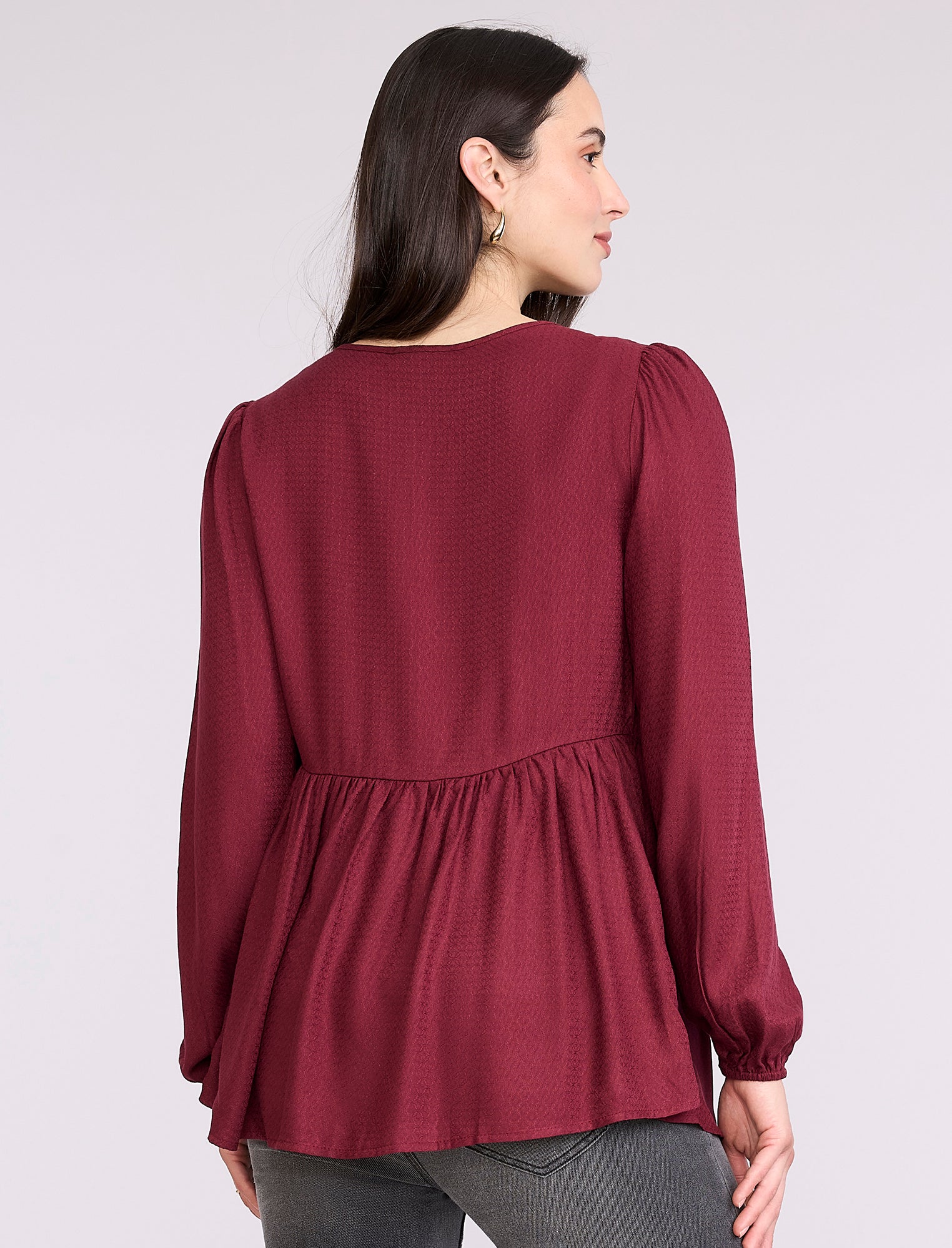 Pregnant woman wearing a burgundy long-sleeve top on a light gray background