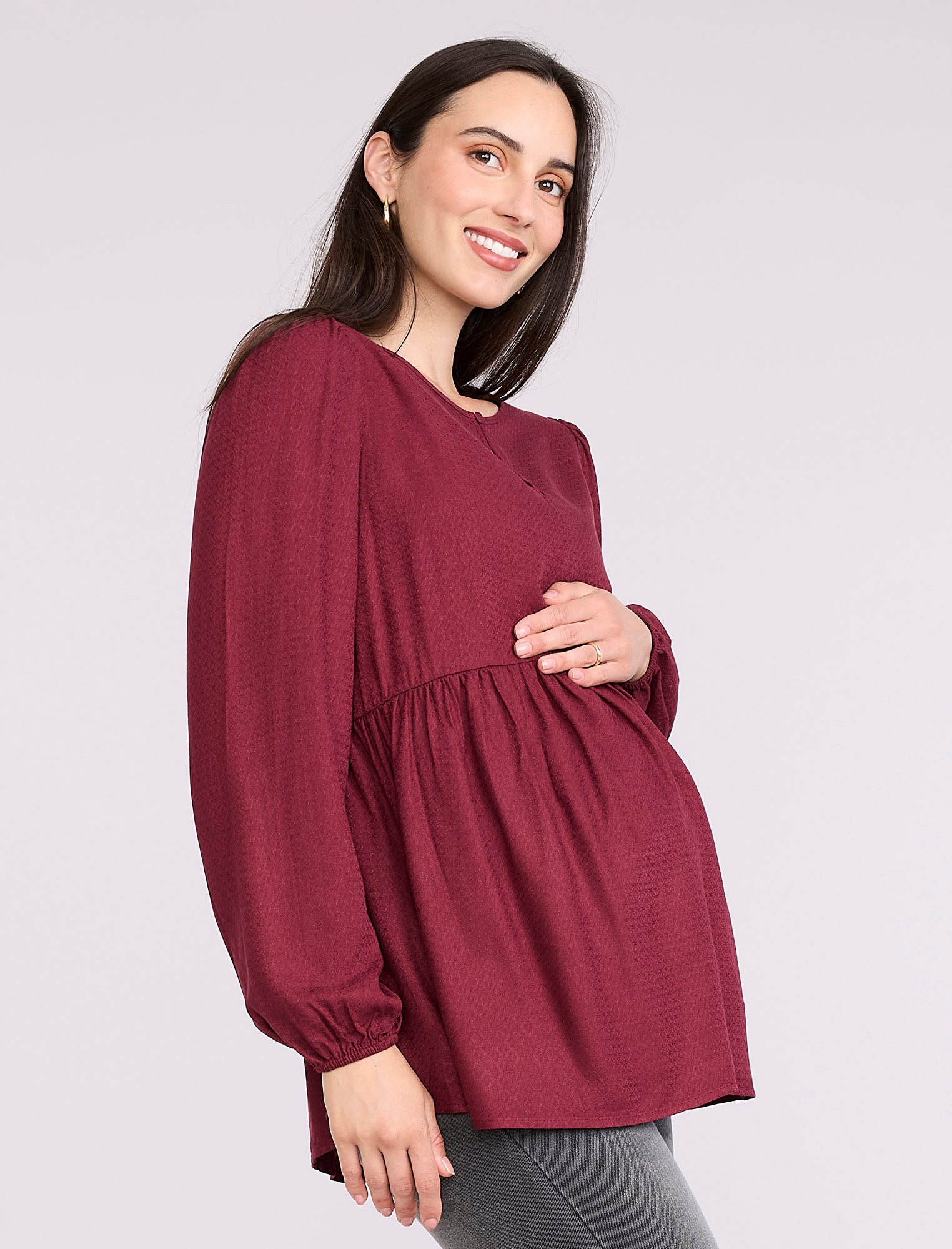 Pregnant woman wearing a burgundy long-sleeve top on a light gray background
