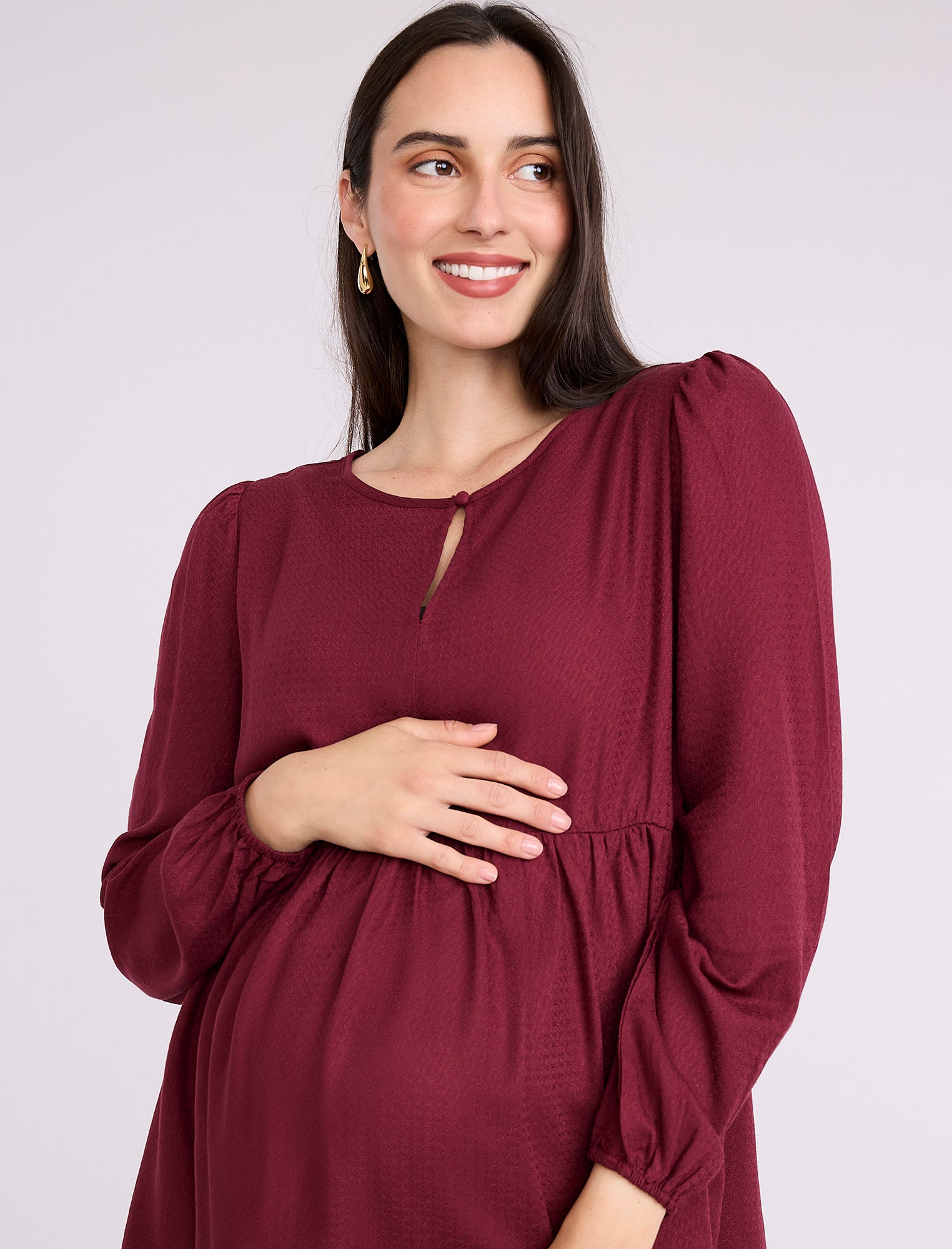 Pregnant woman wearing a burgundy long-sleeve top on a light gray background