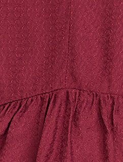 Pregnant woman wearing a burgundy long-sleeve top on a light gray background