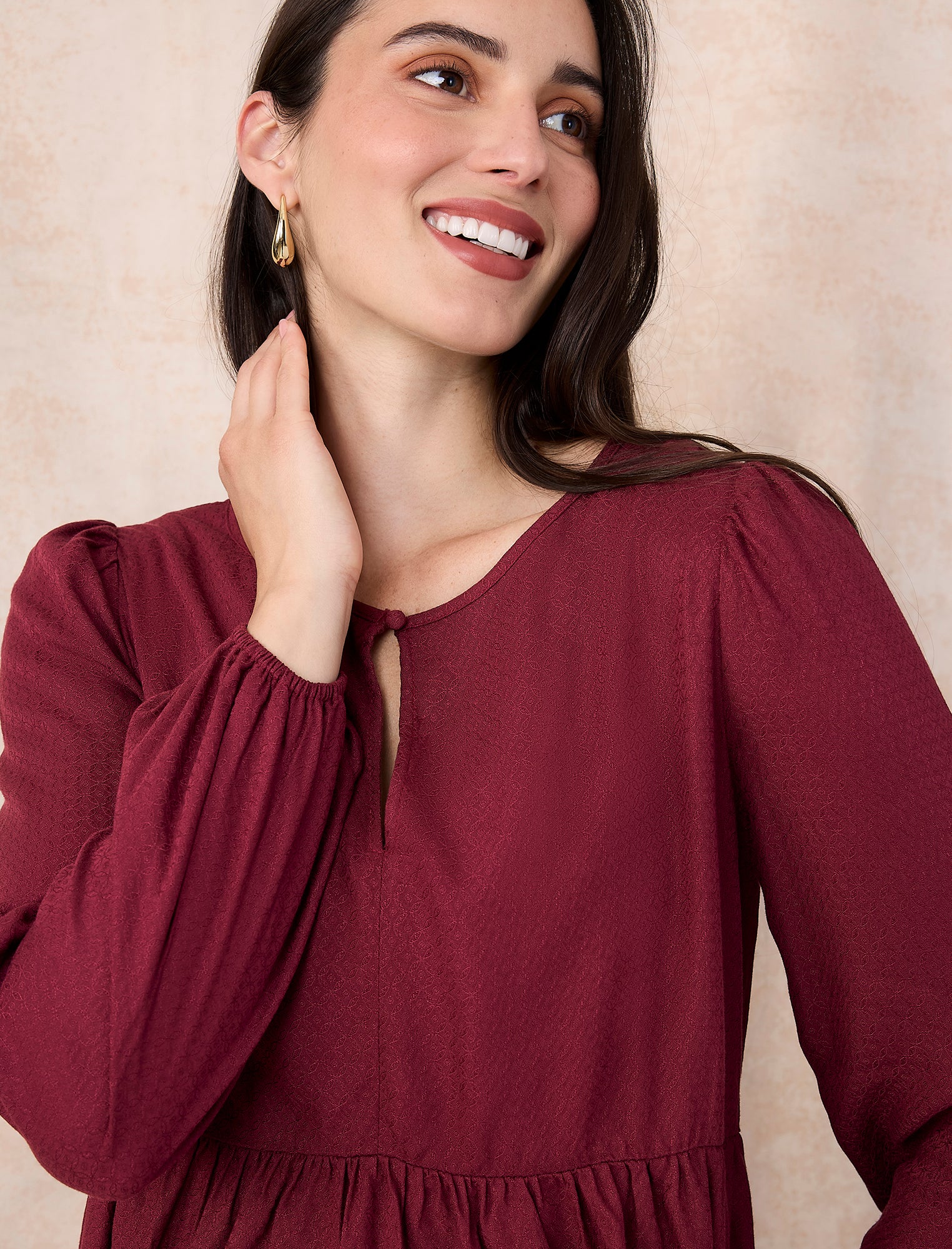 Pregnant woman wearing a burgundy long-sleeve top on a light gray background