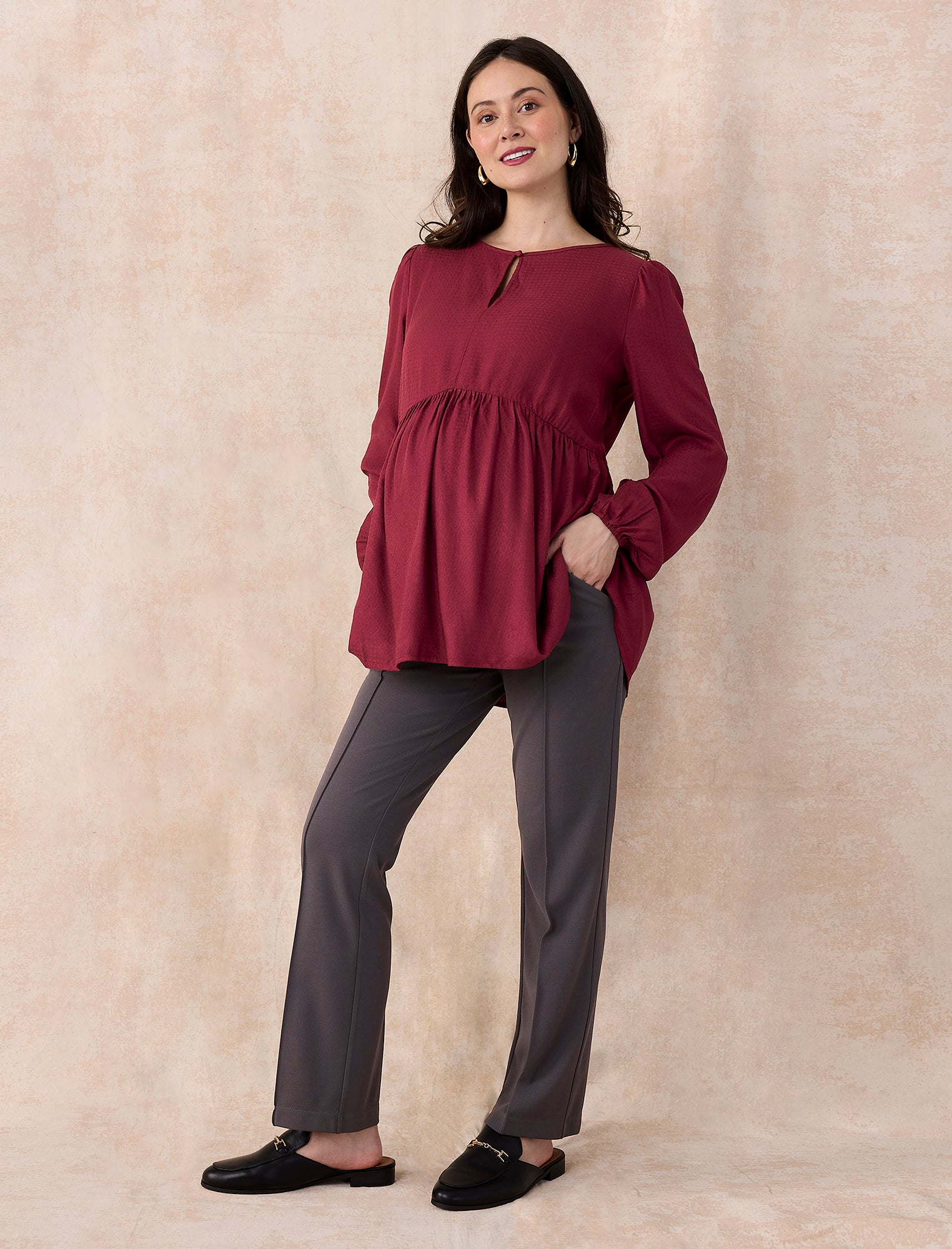 Pregnant woman wearing a burgundy long-sleeve top on a light gray background