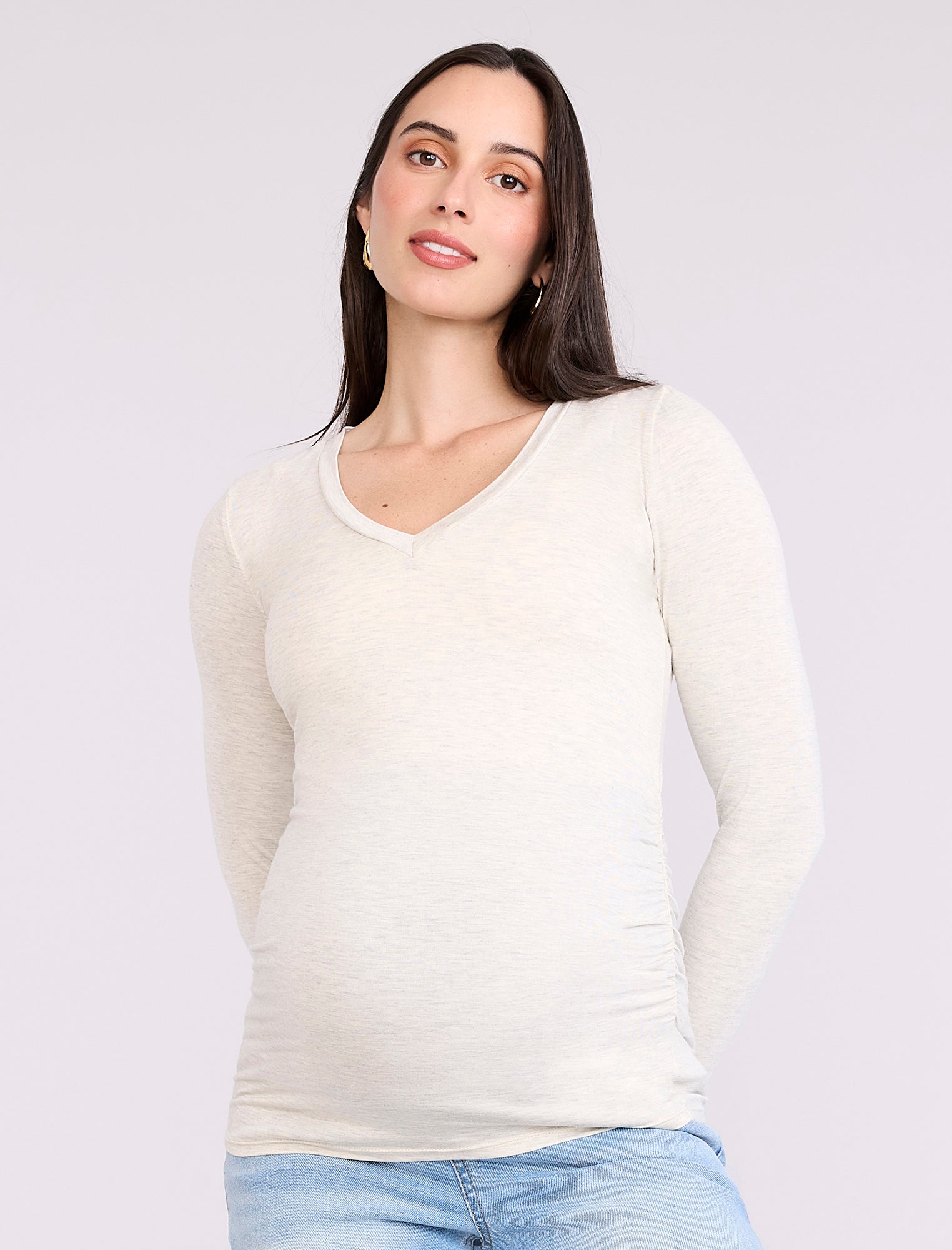 Pregnant woman wearing an off-white long-sleeve maternity top against a plain background