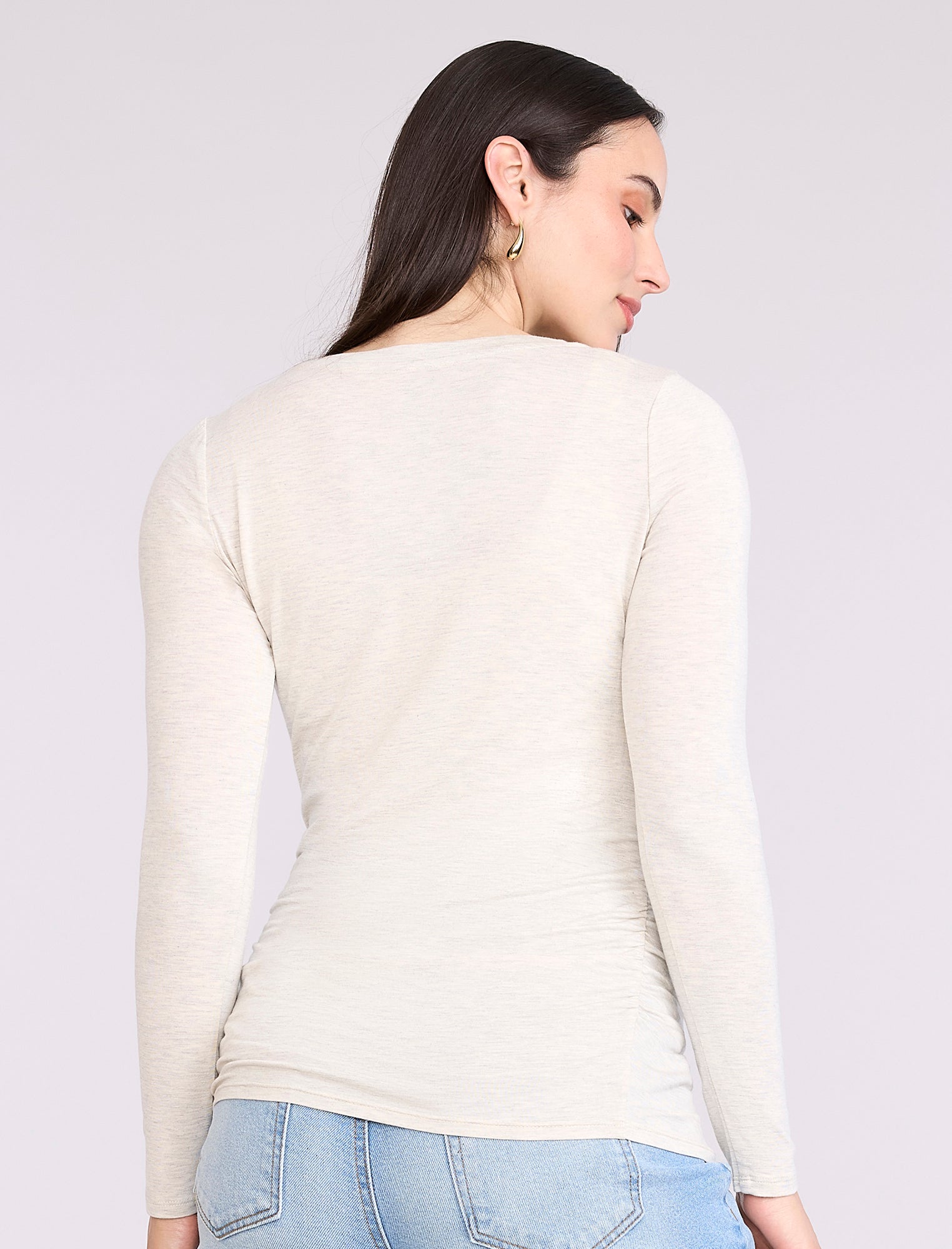 Pregnant woman wearing an off-white long-sleeve maternity top against a plain background