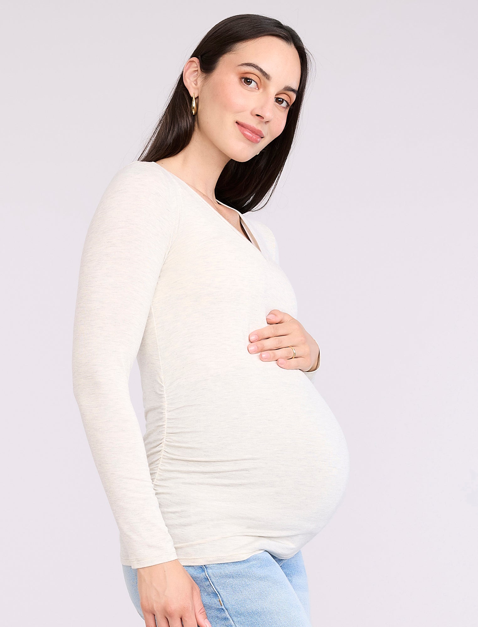 Pregnant woman wearing an off-white long-sleeve maternity top against a plain background